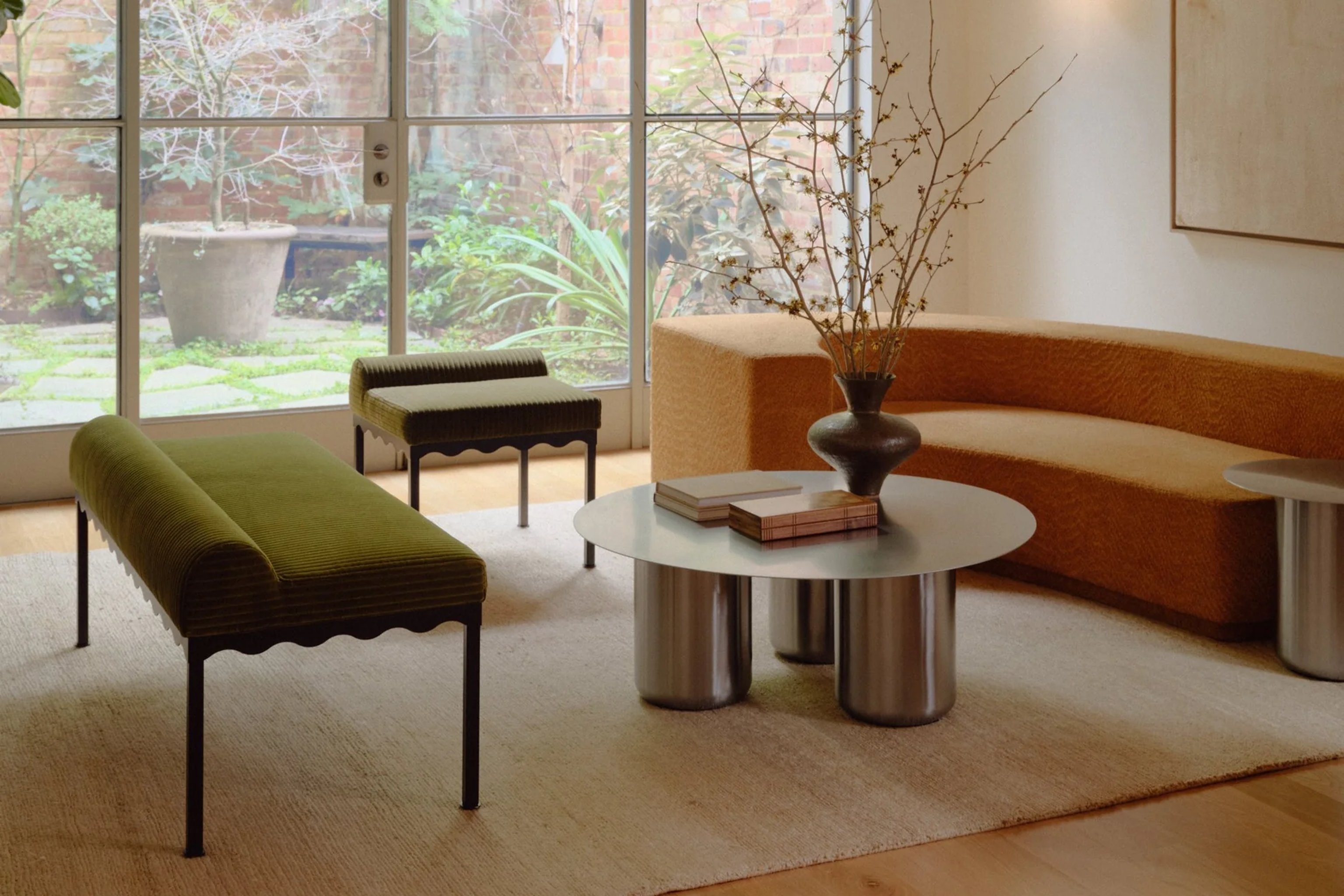 A stainless steel coffee table in a beautiful room with upholstered benches and an orange sofa.