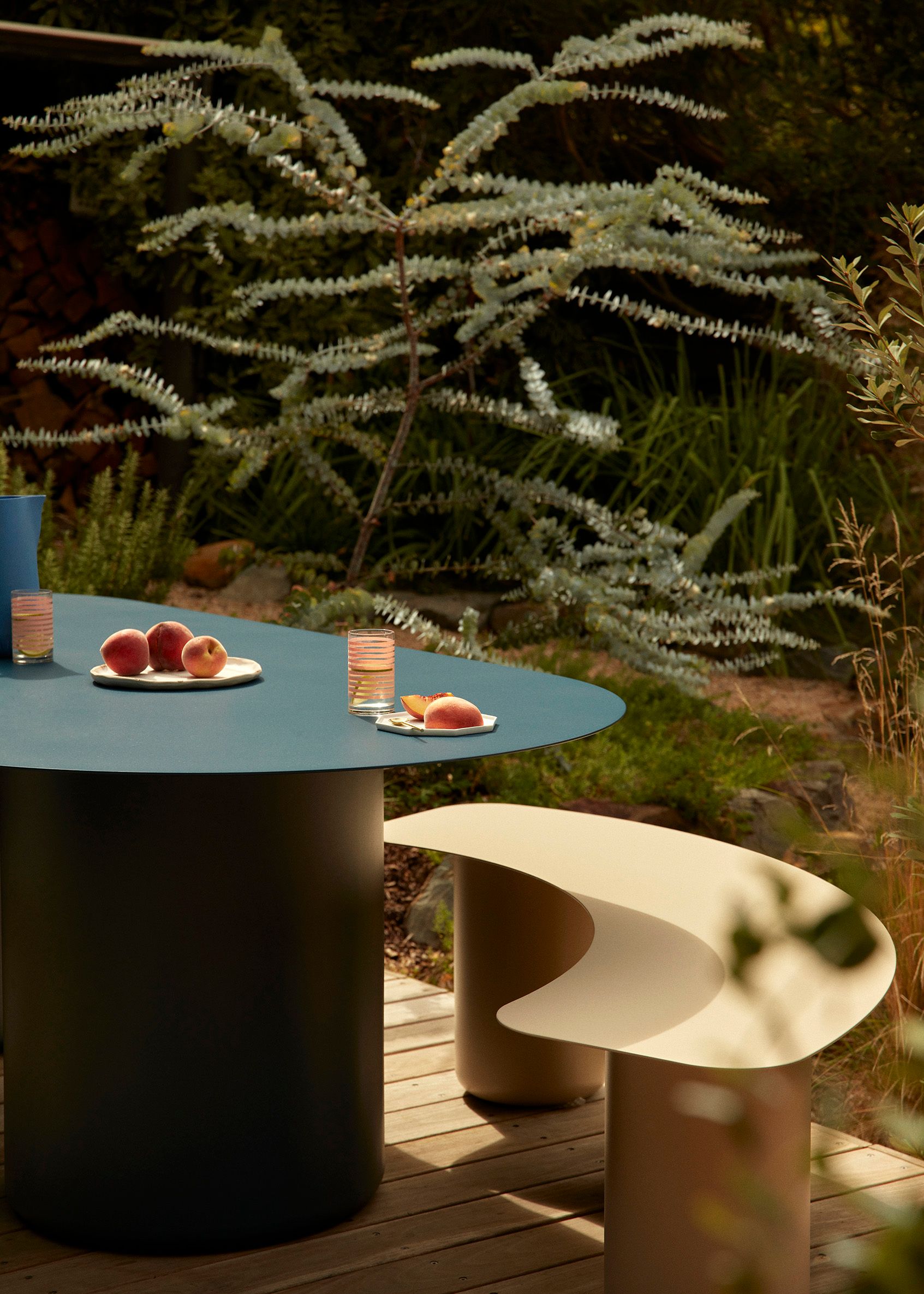 An outdoor dining setting with a blue dining table and beige coloured stool made from steel