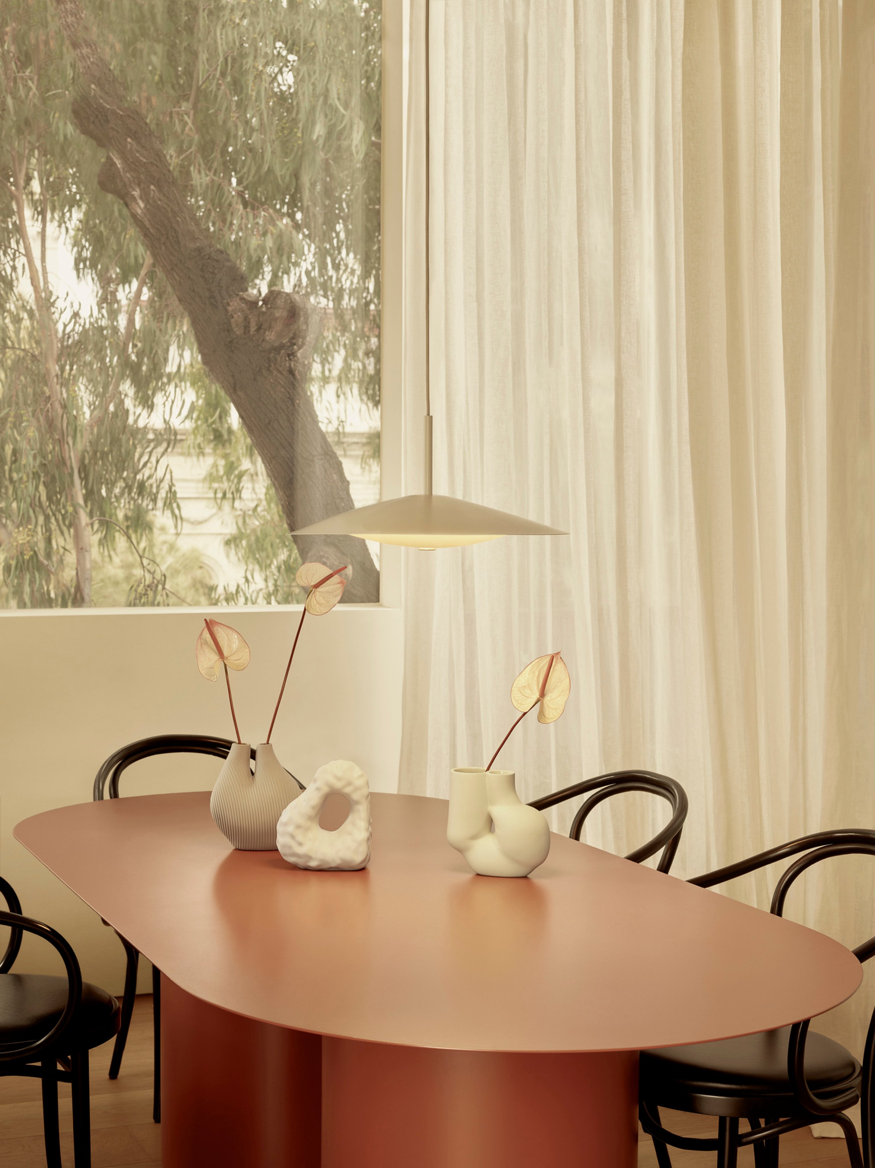 A streamlined white pendant light glows above a red oval dining table with black bentwood chairs.