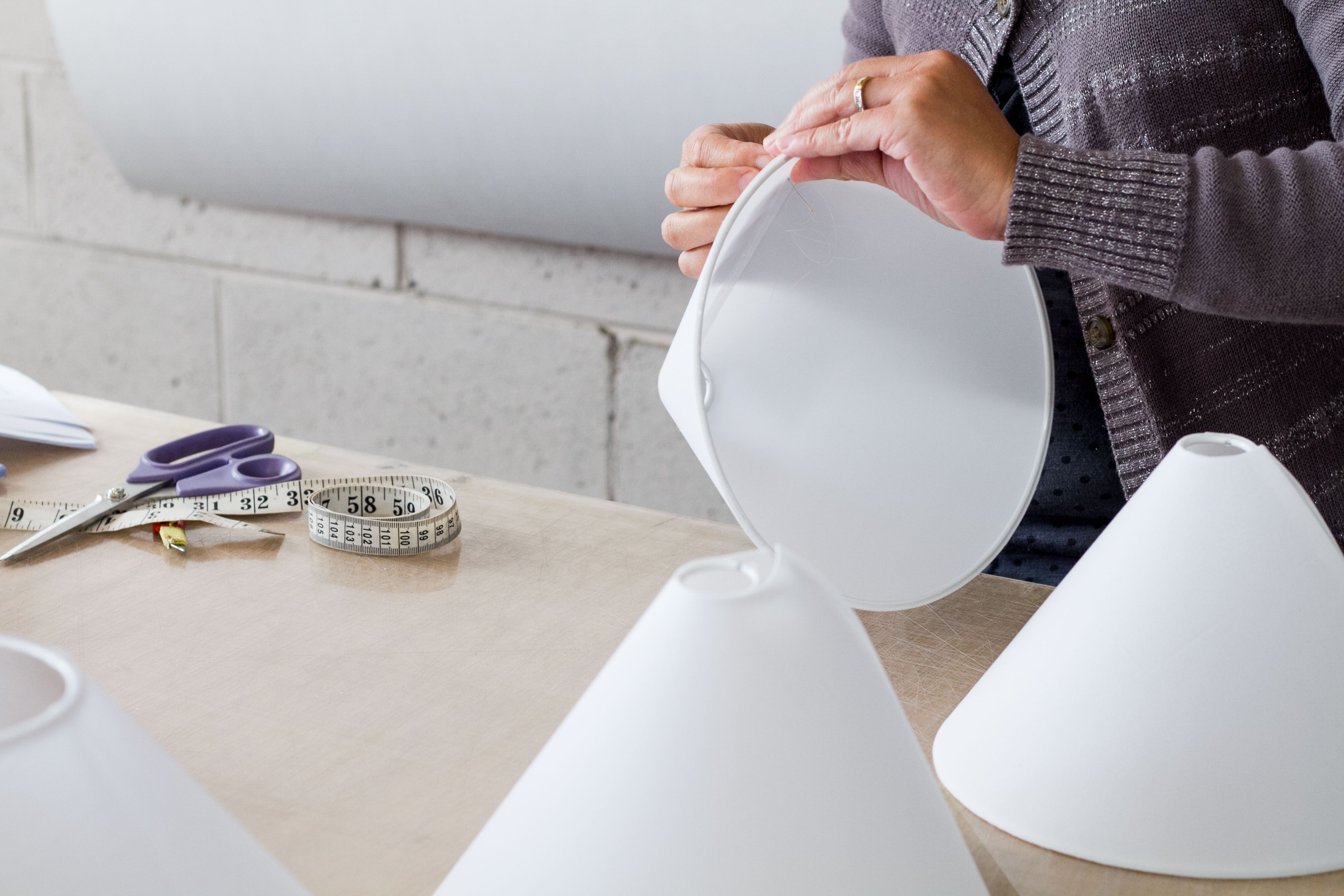 Hands applying tape to a fabric shade stretched around a wire frame