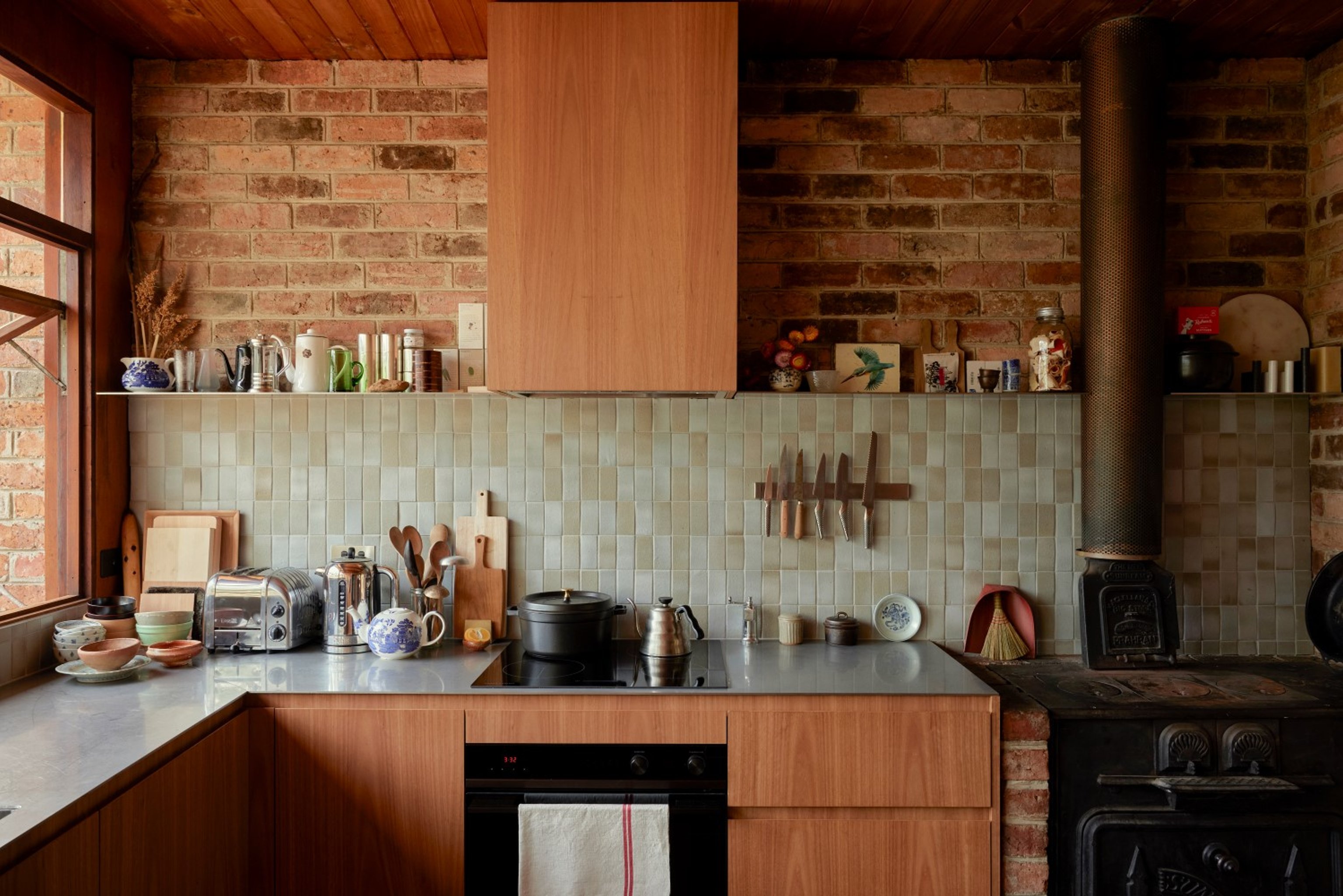 A lived in kitchen with warm timber cabinetry, pale green tiled splashback and stainless steel benchtops