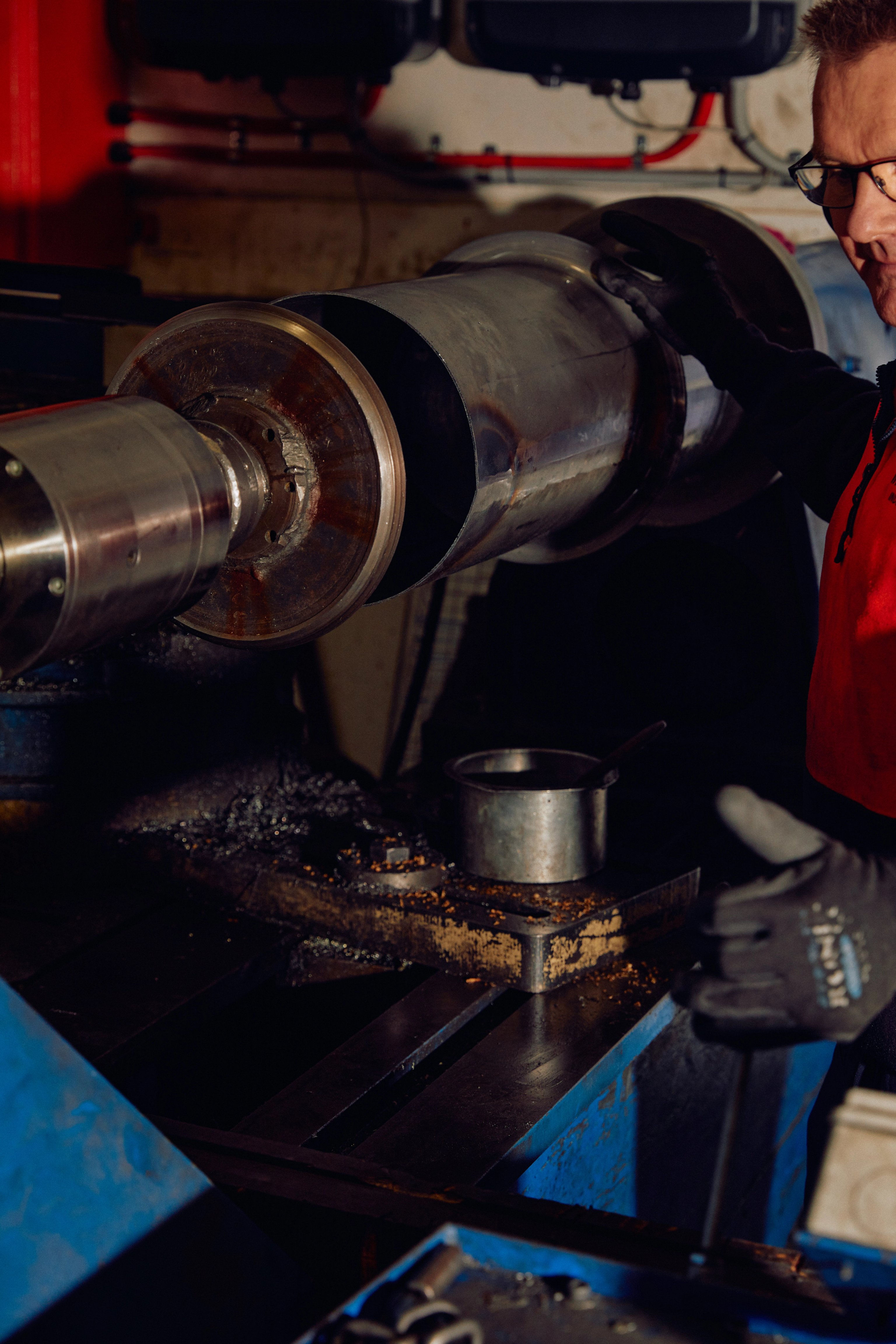 A man stands next to a metal lathe in an industrial factory