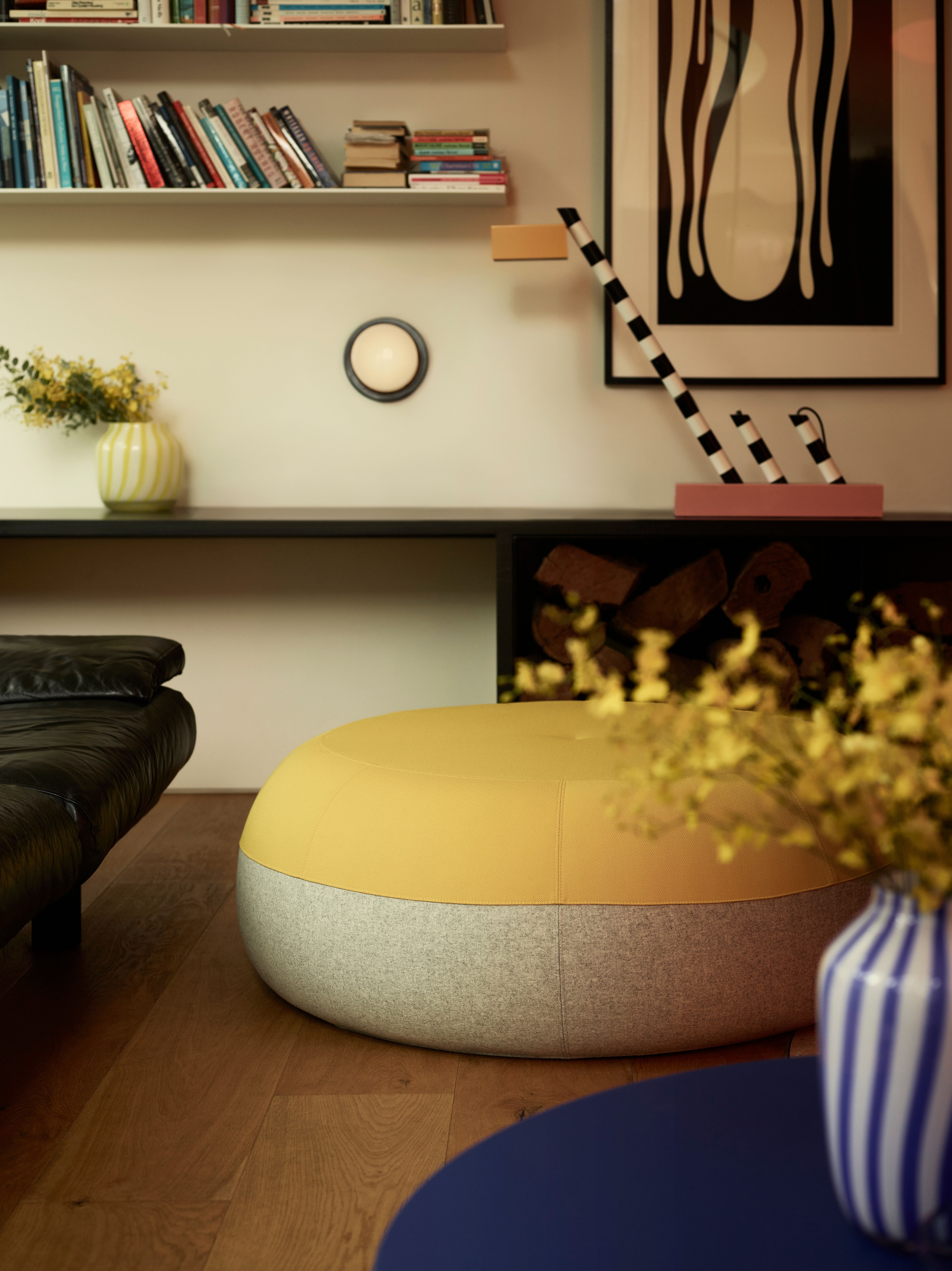 A warm living room scene, with a large yellow Puku ottoman and Honey wall light.