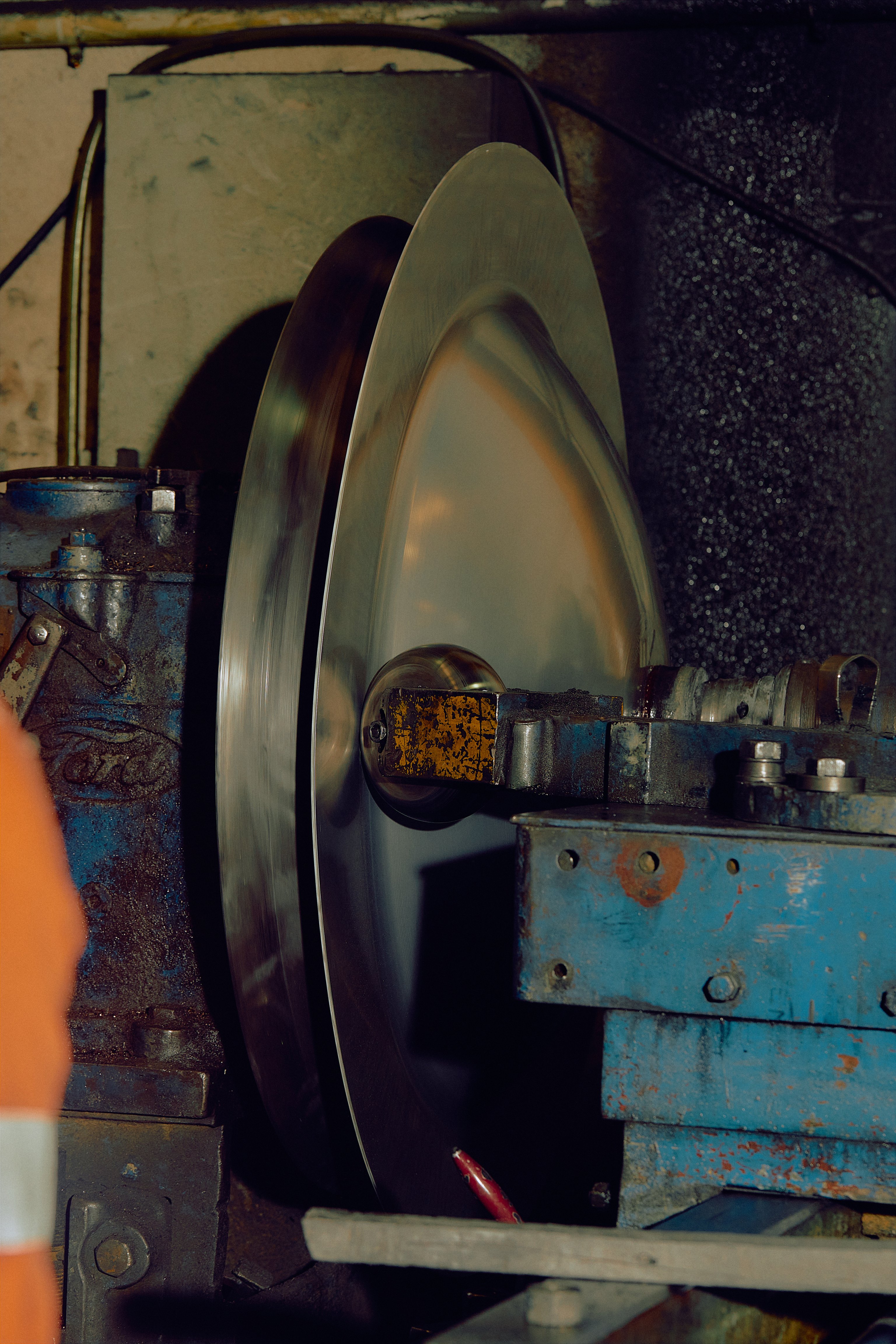 A large metal disk being spun by a wheel on a lathe in an industrial factory.