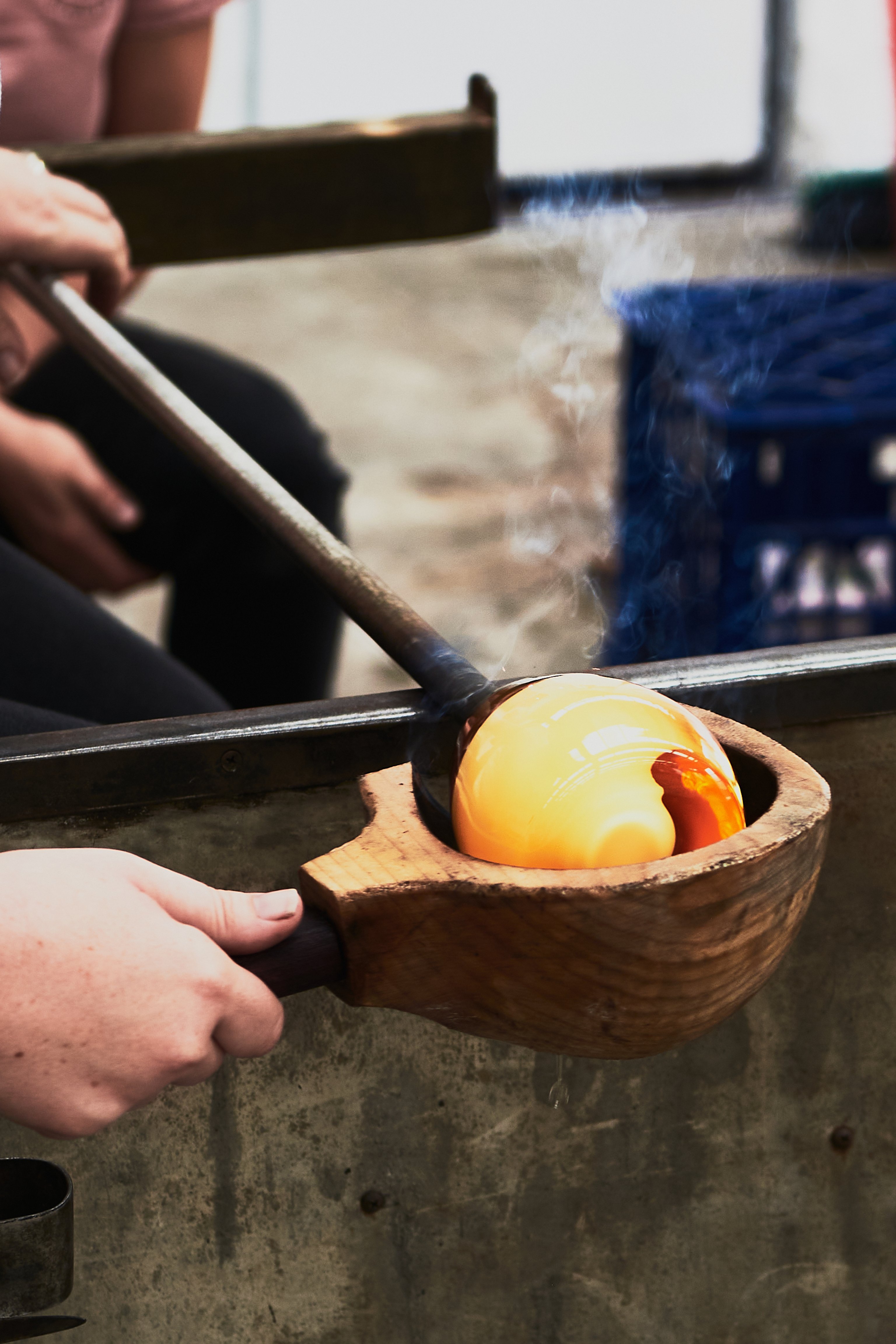 A rounded timber mould cups an orange ball of glass on a blow tube.