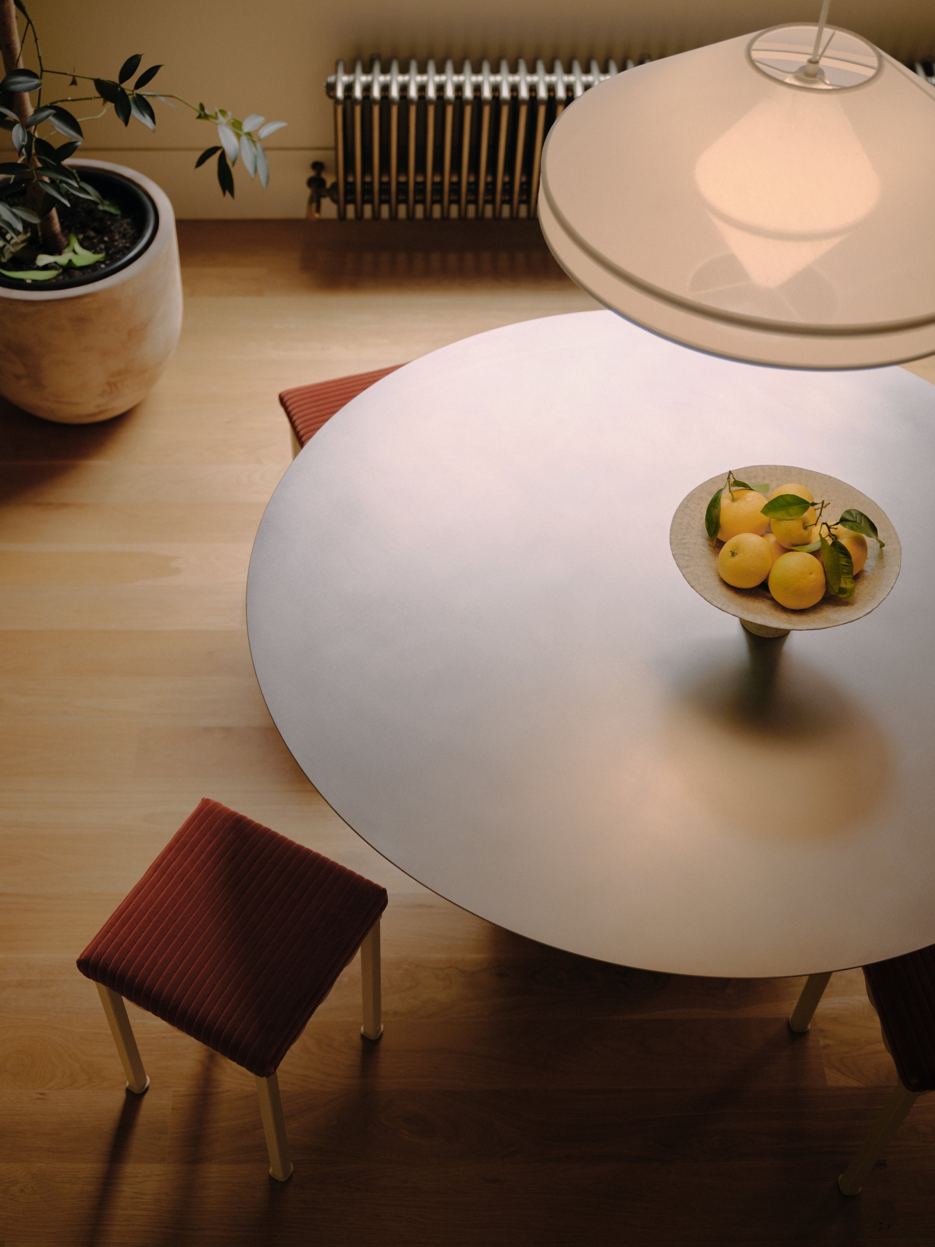 A stainless steel dining table top with red upholstered stools and a fabric mesh pendant light