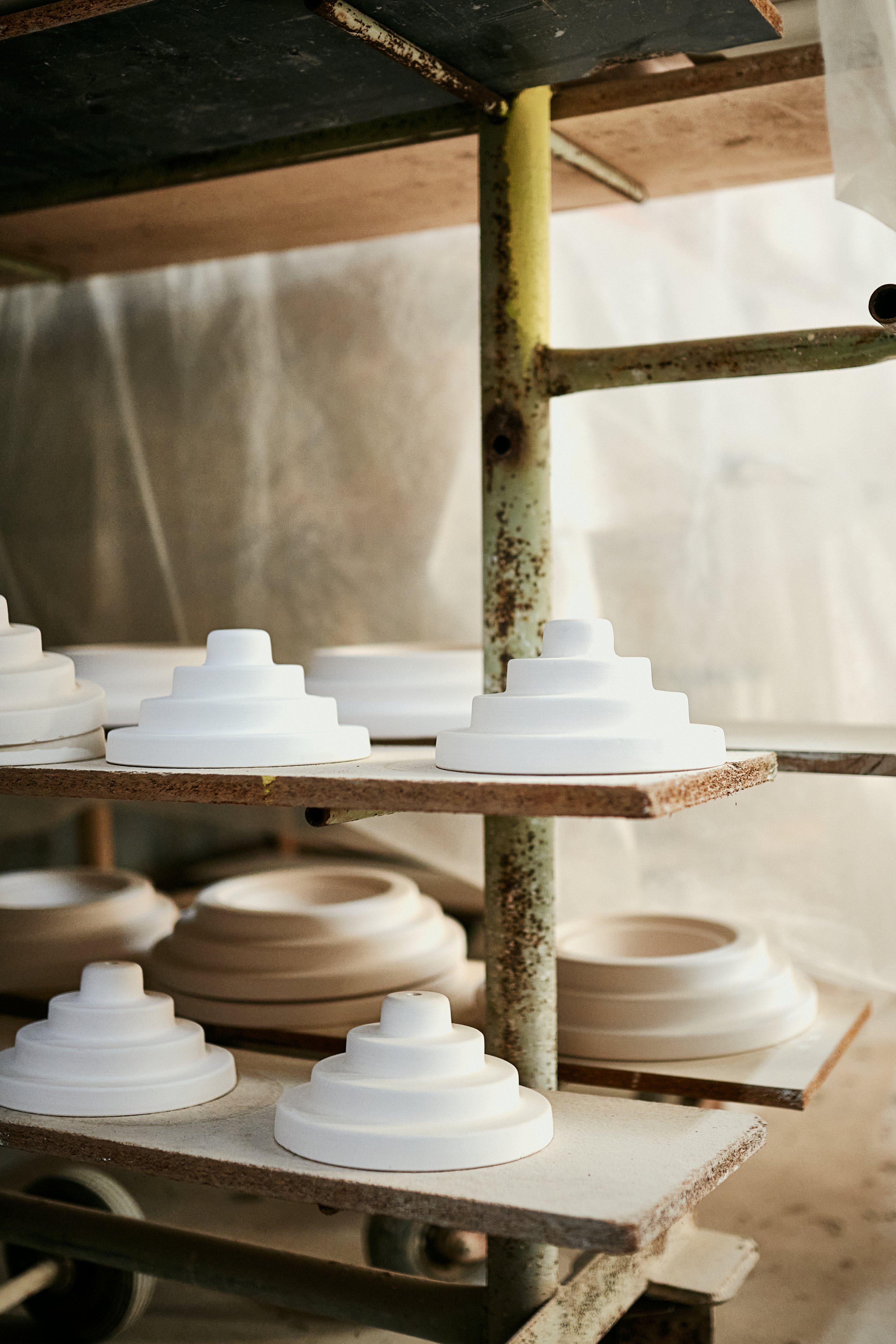 A batch of ceramic Honey pendant lights and wall lights sit on a drying rack in a factory.
