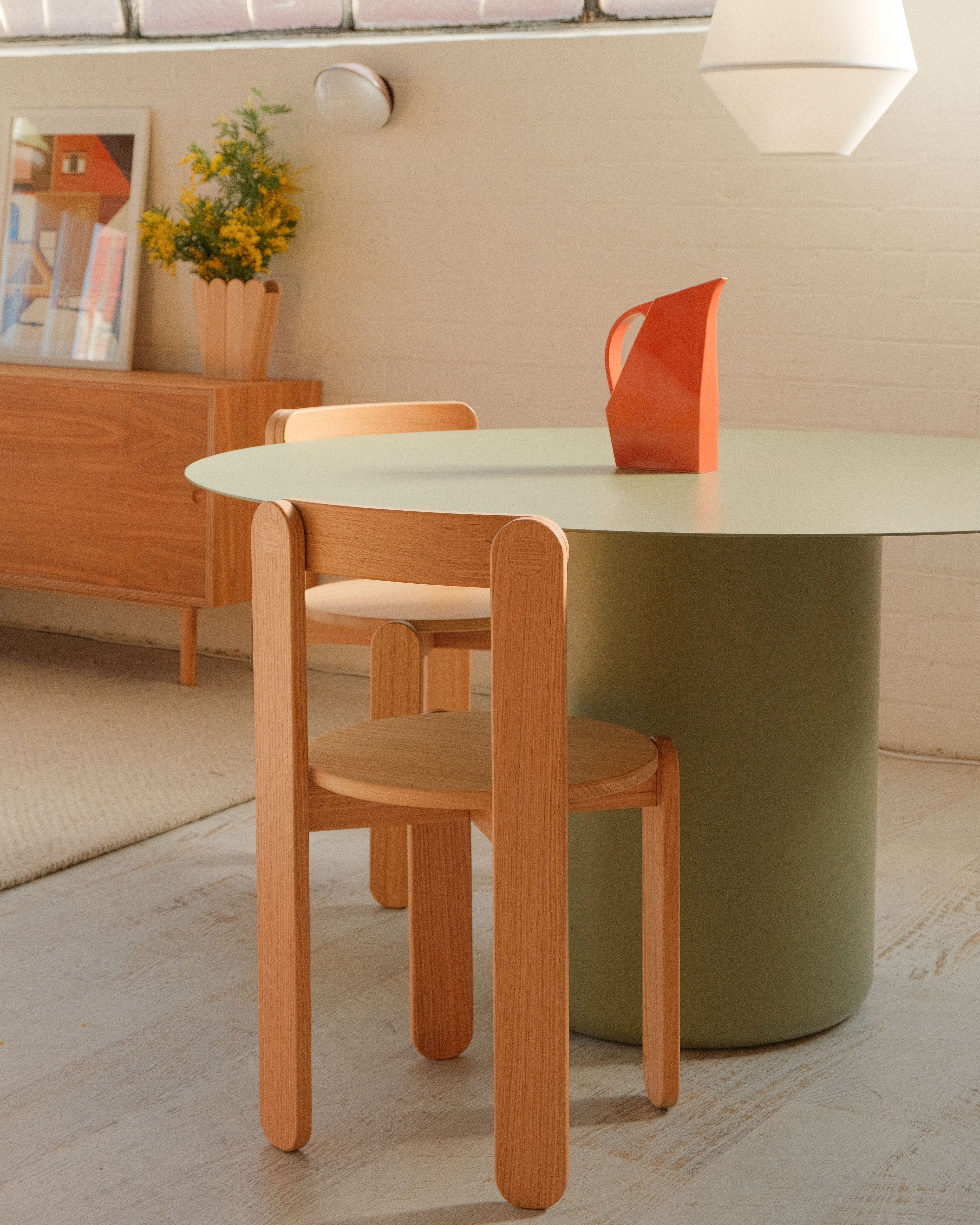 Green Sequence Round Dining Table with timber chairs and a red vase