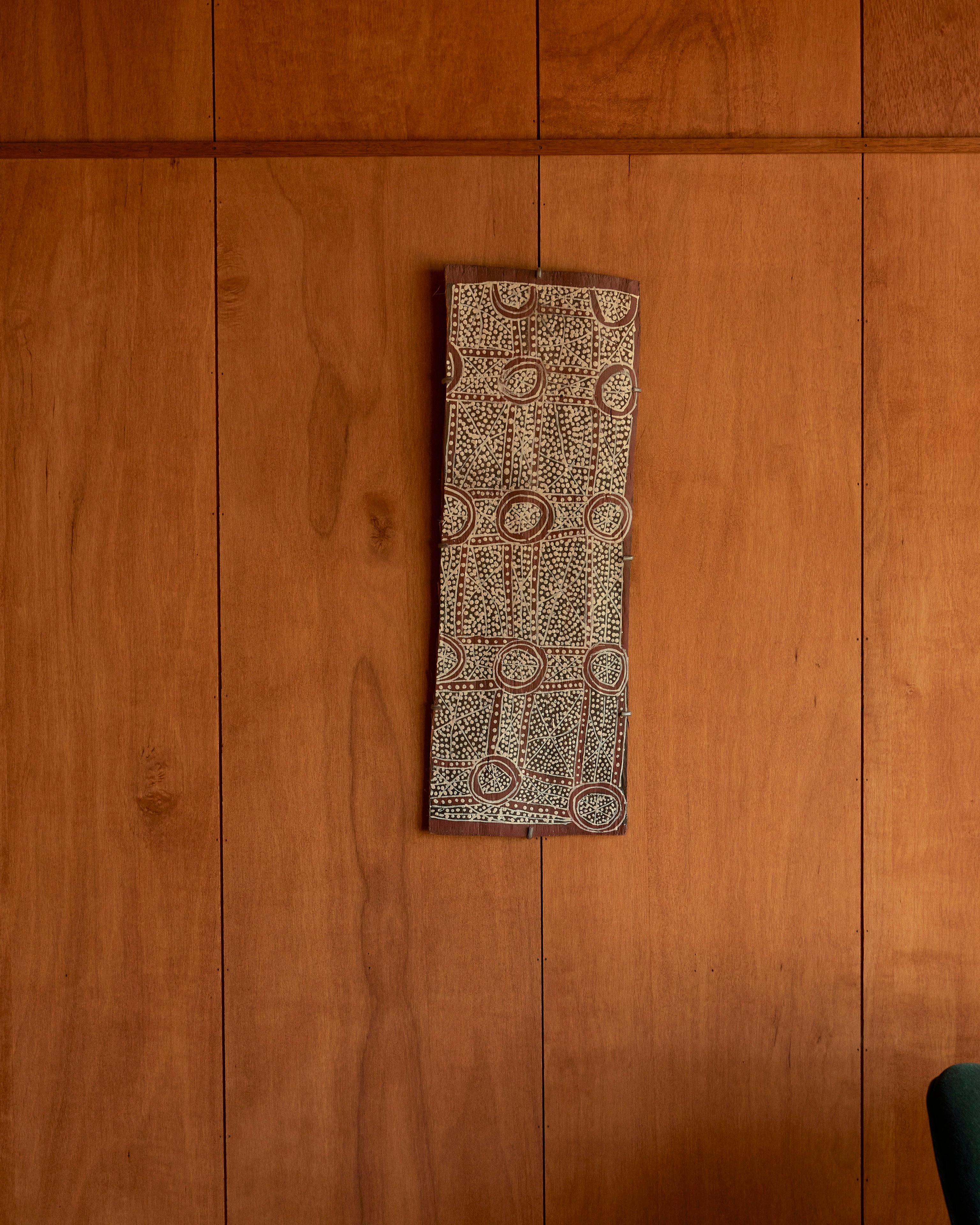 An indigenous painting hung on a timber clad wall