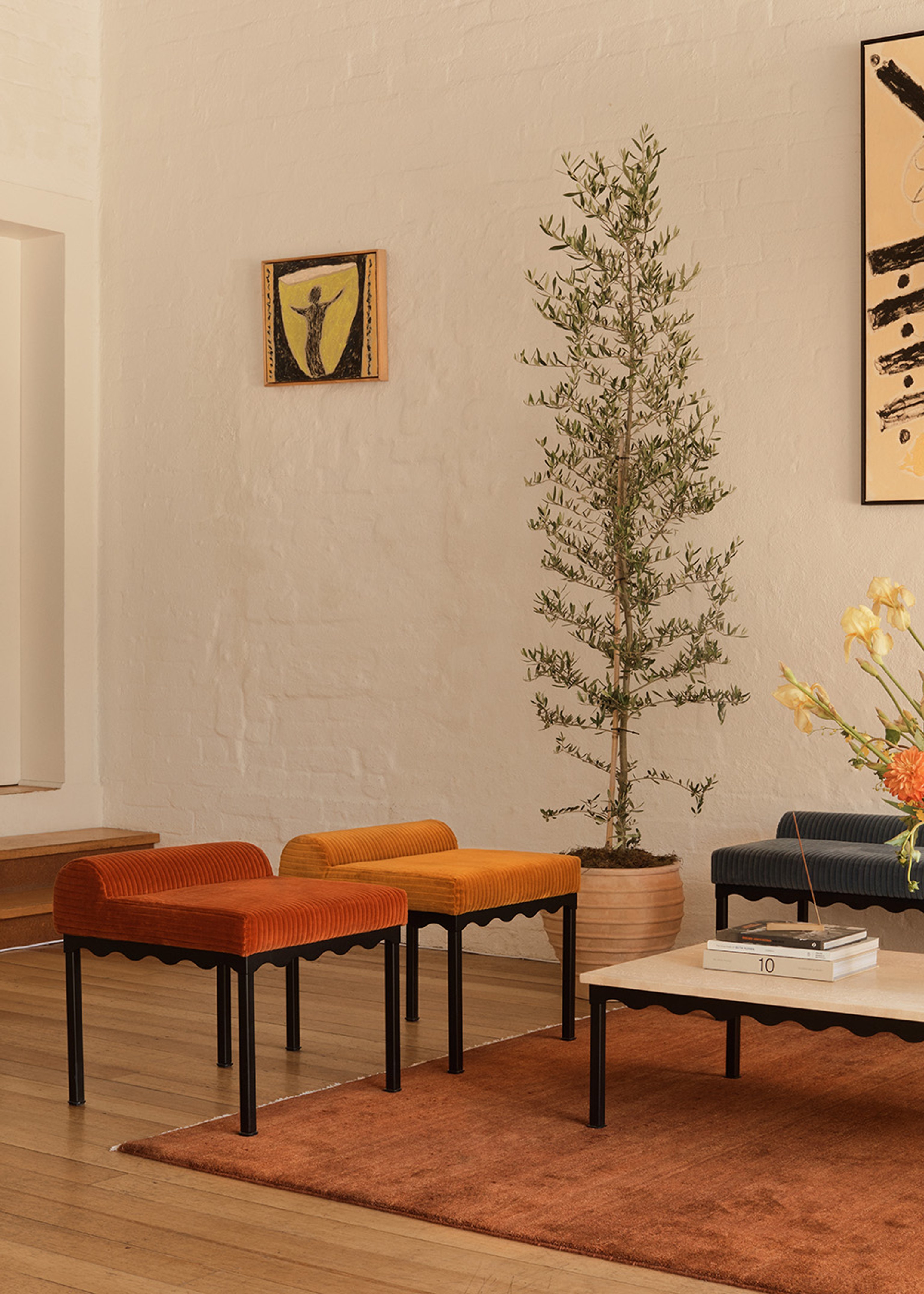 A room with a collection of Coco Flip furniture pieces and a small artwork. In the room you can see two upholstered benches with red and yellow corduroy seats