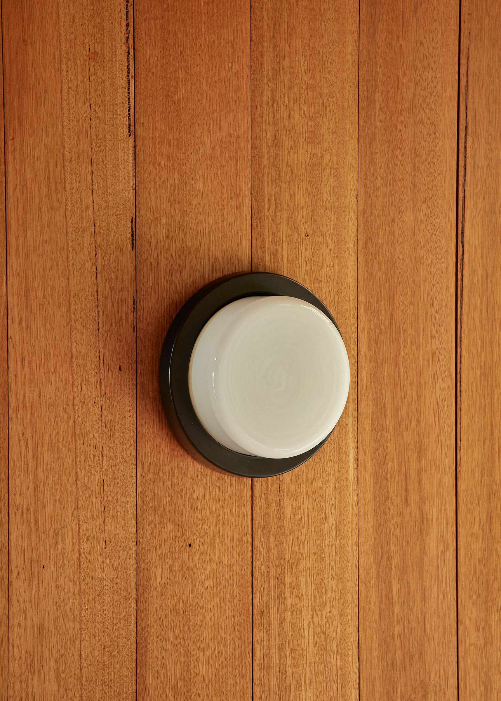 A single rimmed Honey Wall Light with a black ceramic slip-cast base and hand-blown glass diffuser