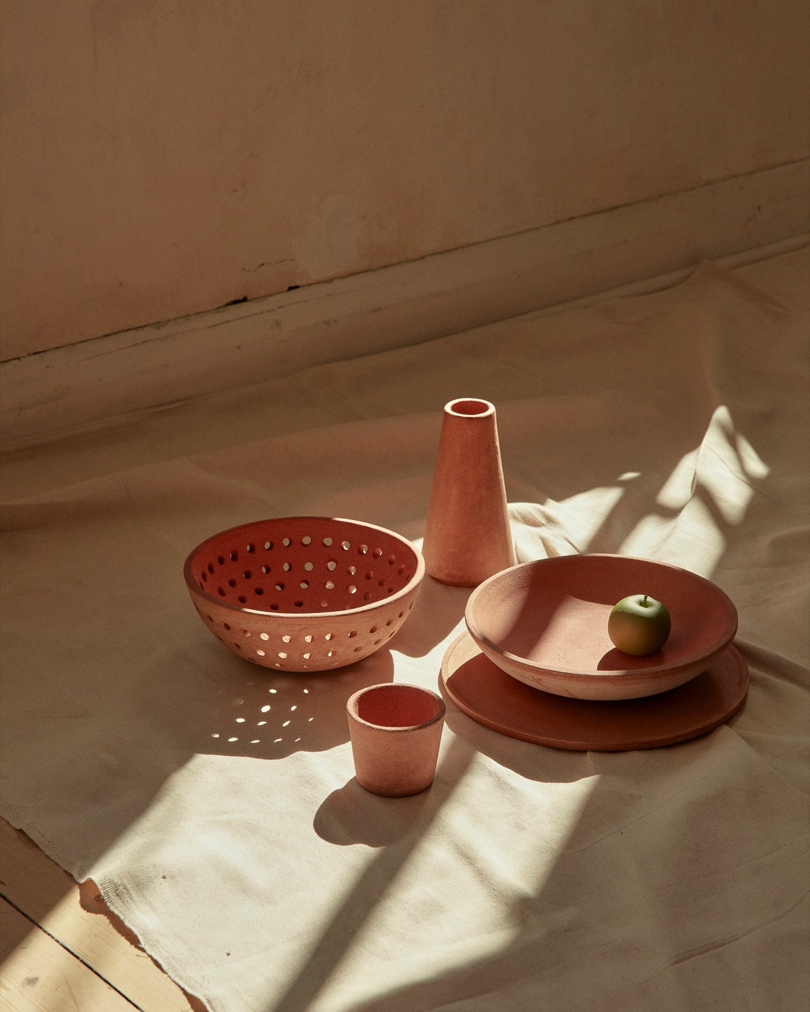 A collection of terracotta objects designed for New Volumes. Neutral background with strong shadows casting across the items