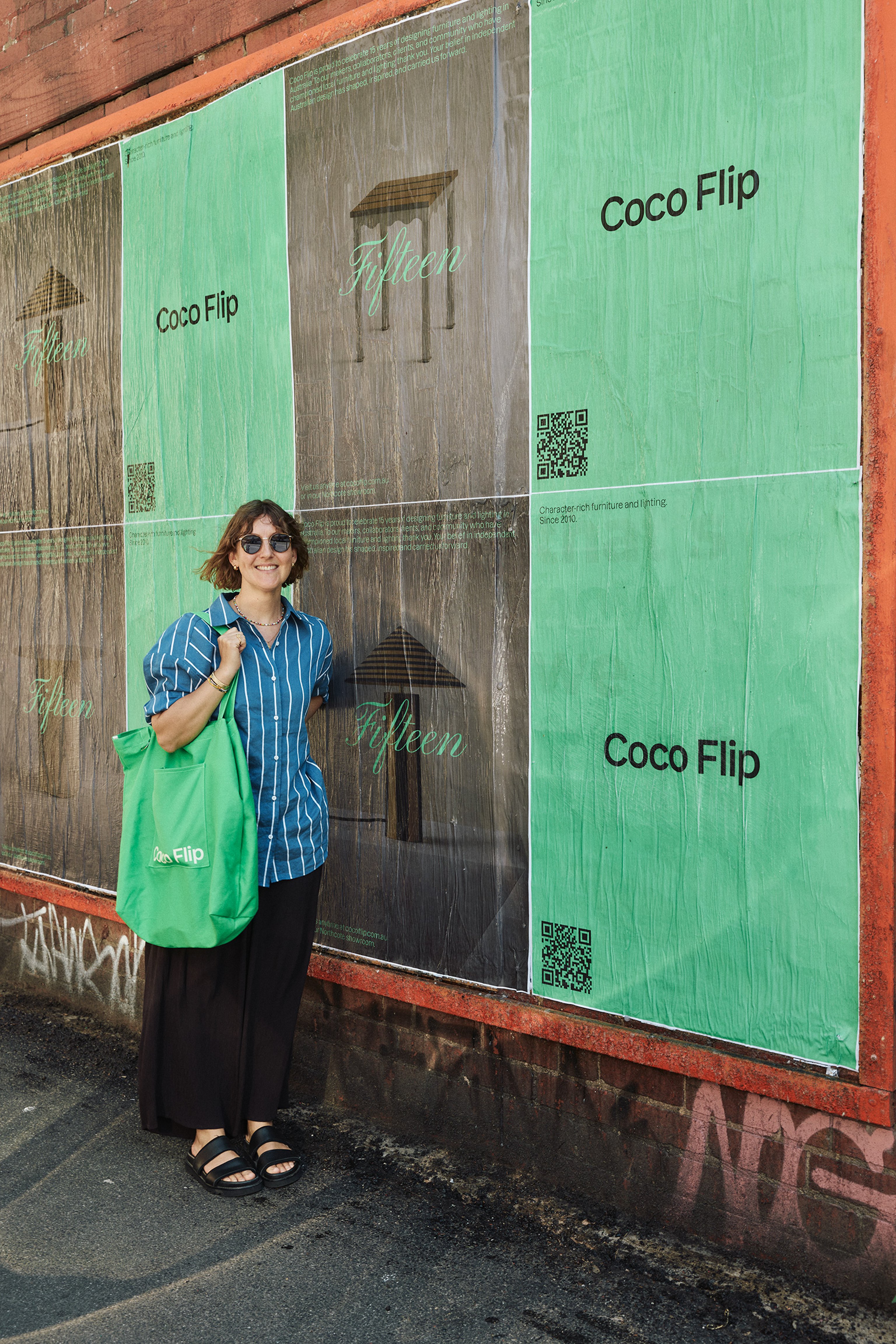 Kate Stokes standing in front of the street posters celebrating 15-years of Coco Flip