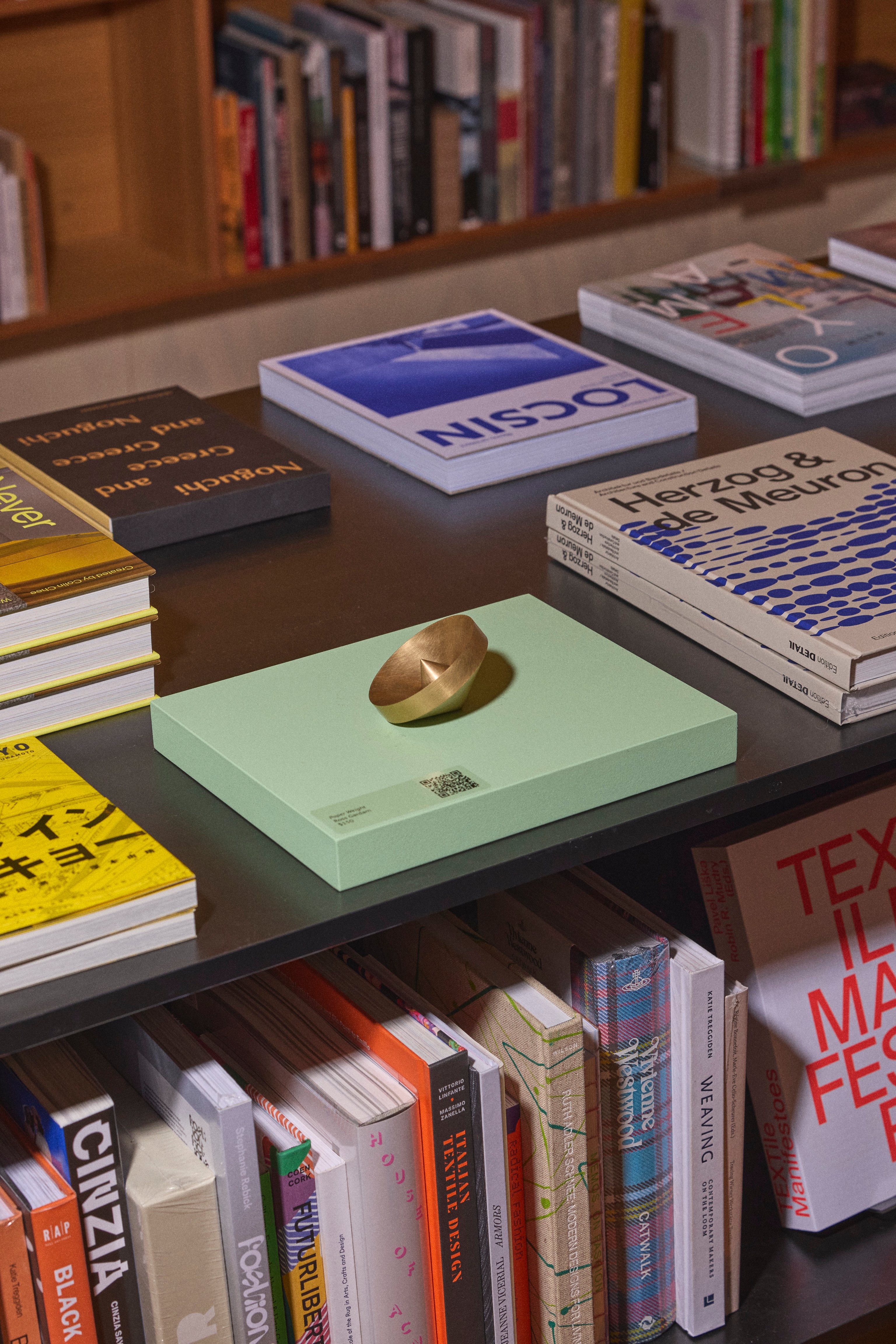A brass paper weight designed for Melbourne Design Week 2024, sitting on a pale green book