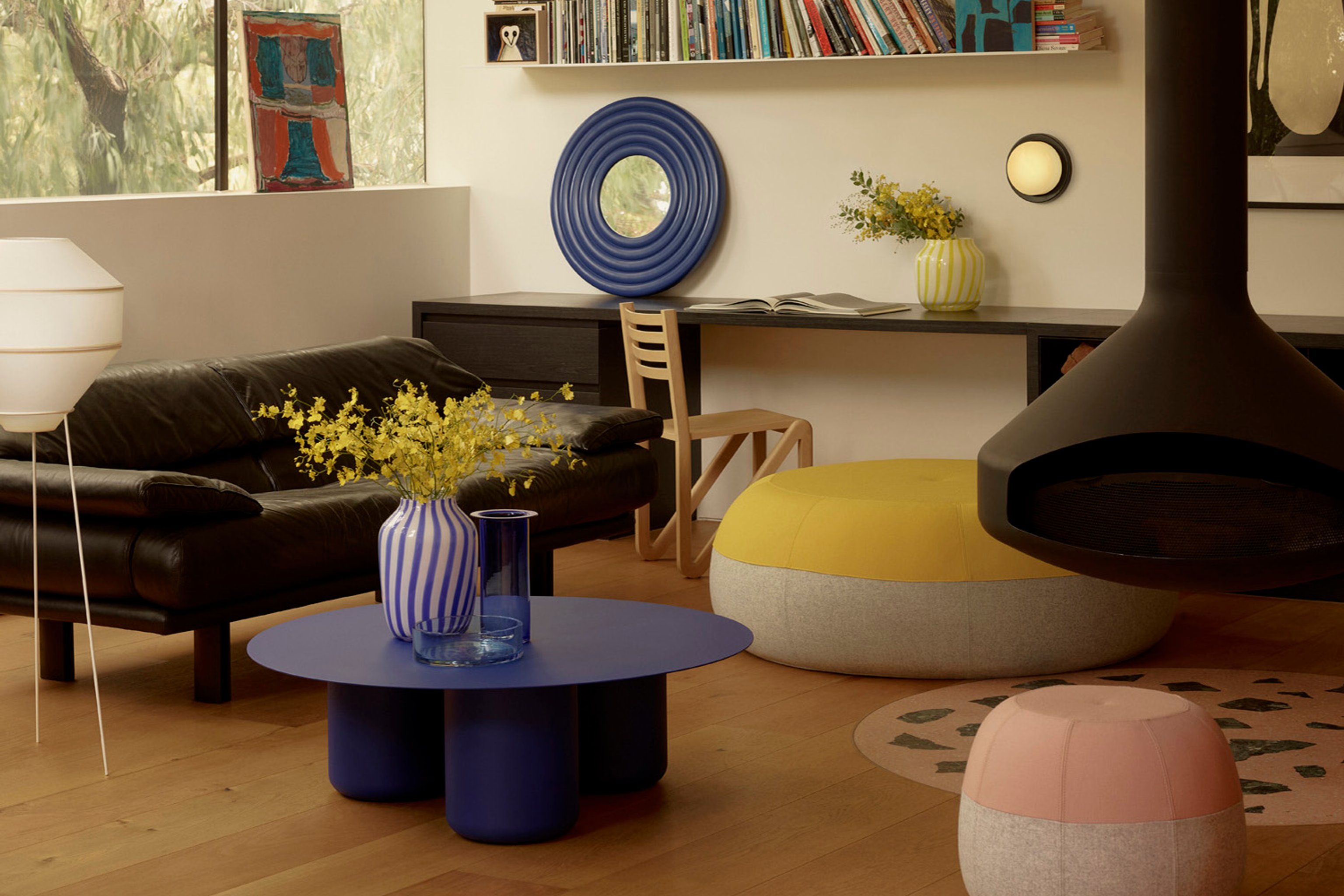 A character filled living room with vivid blue steel coffee table, black sofa and yellow and pink ottomans