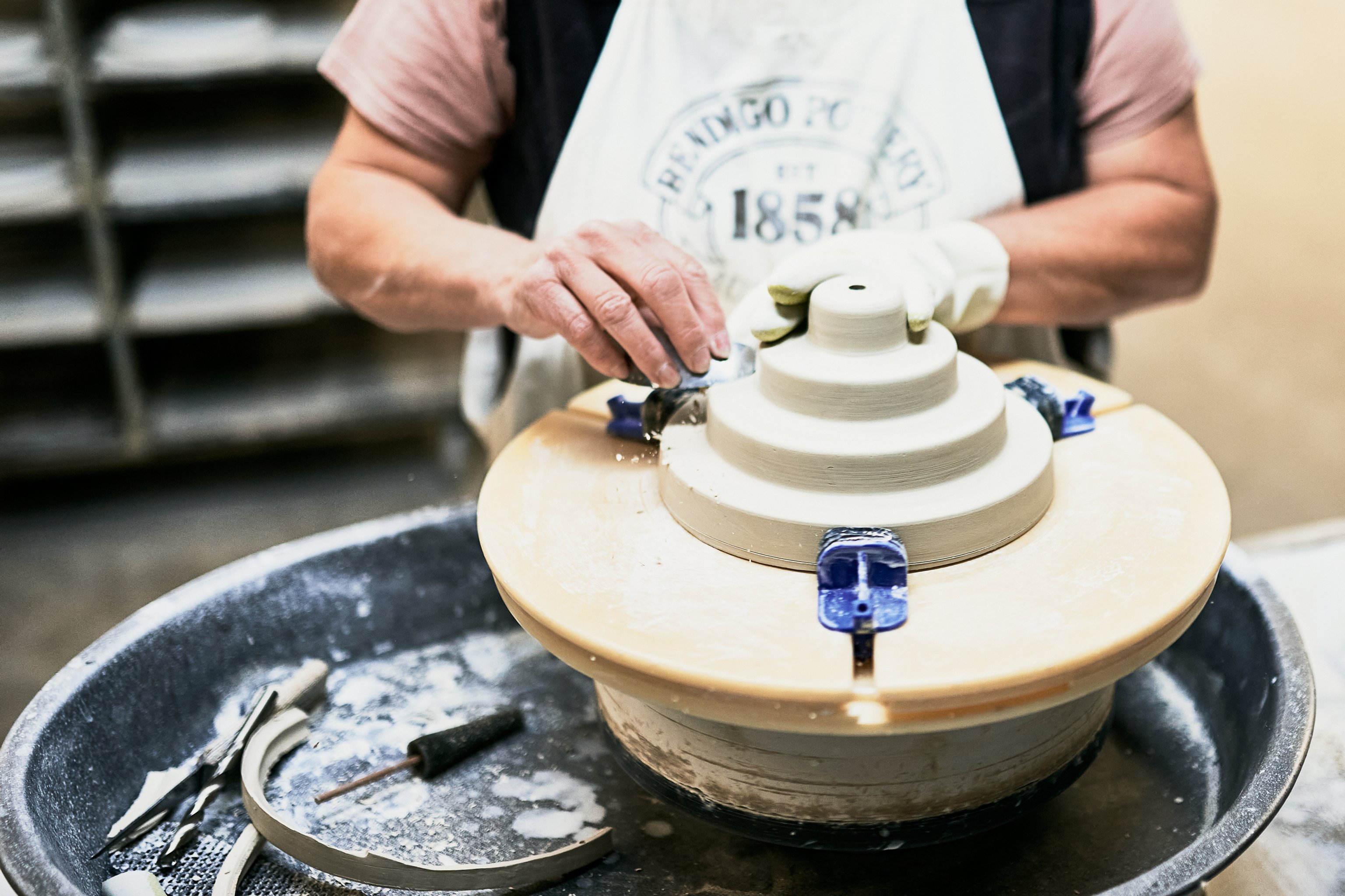 A ceramic Honey pendant component being sanded and trimmed by hand on a wheel.