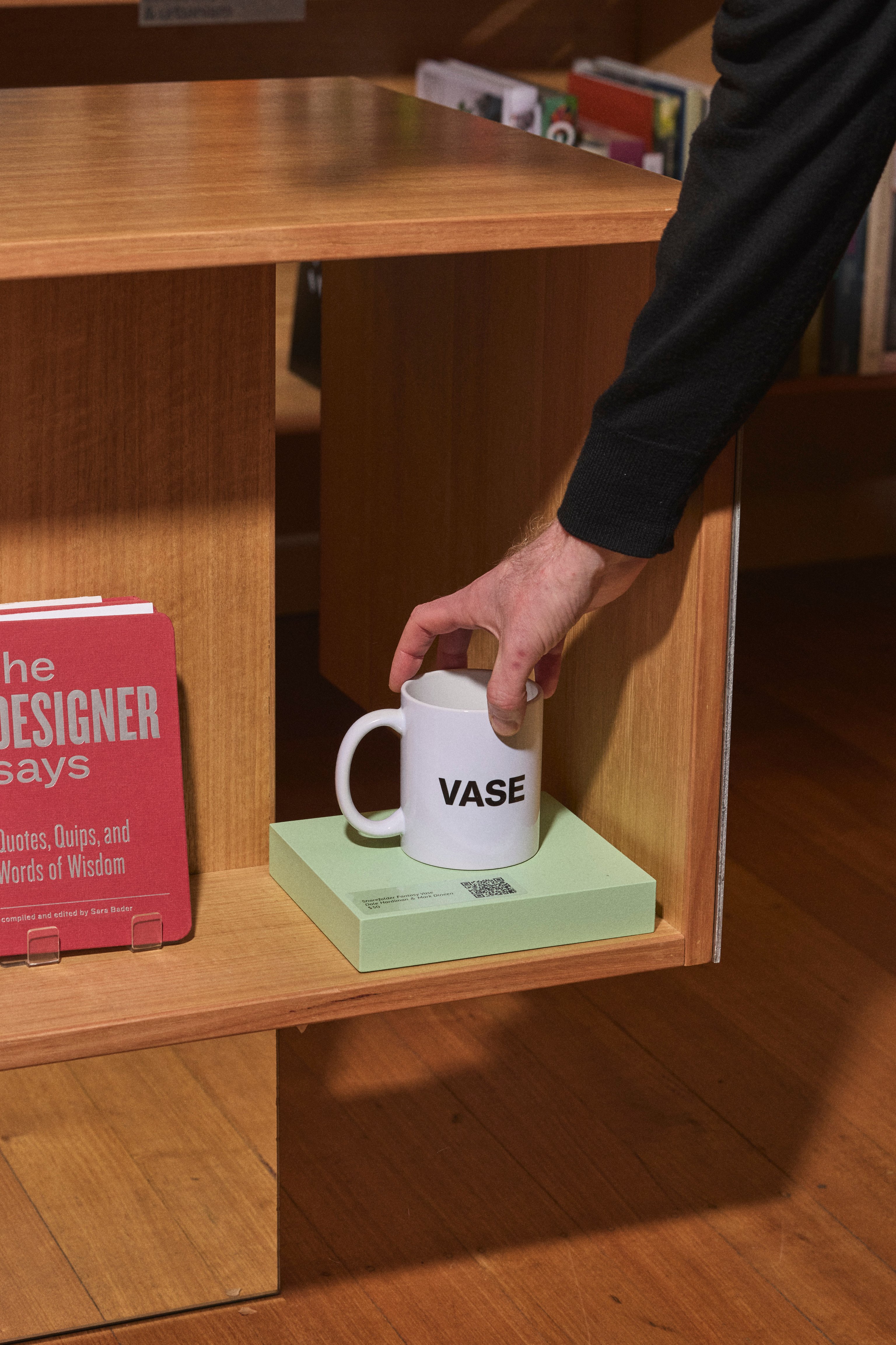 A persons arm reaching to grab a white mug with 'vase' text printed on it