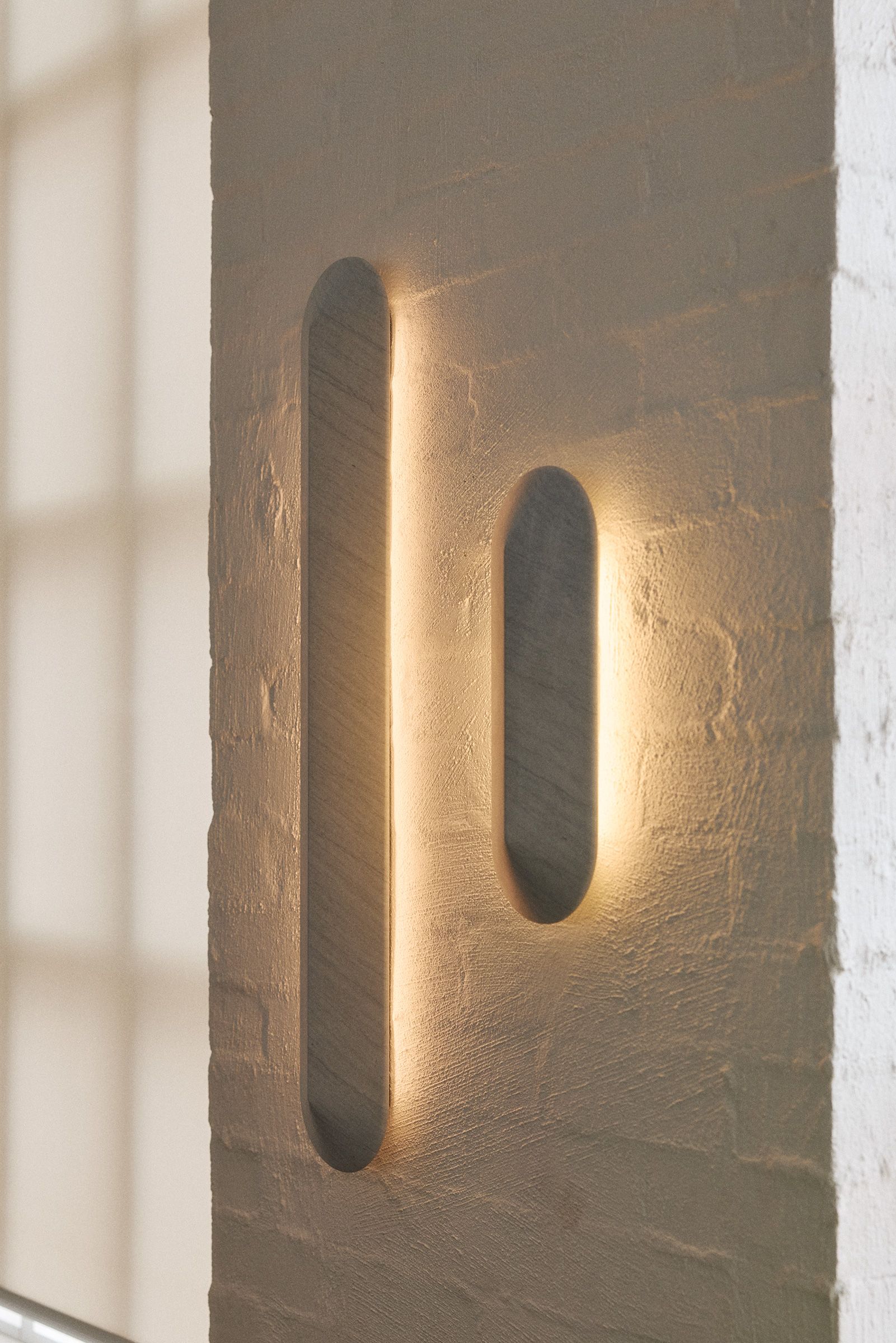 Two Elba Marble Pinch Wall Lights glowing, installed on a white rendered brick wall