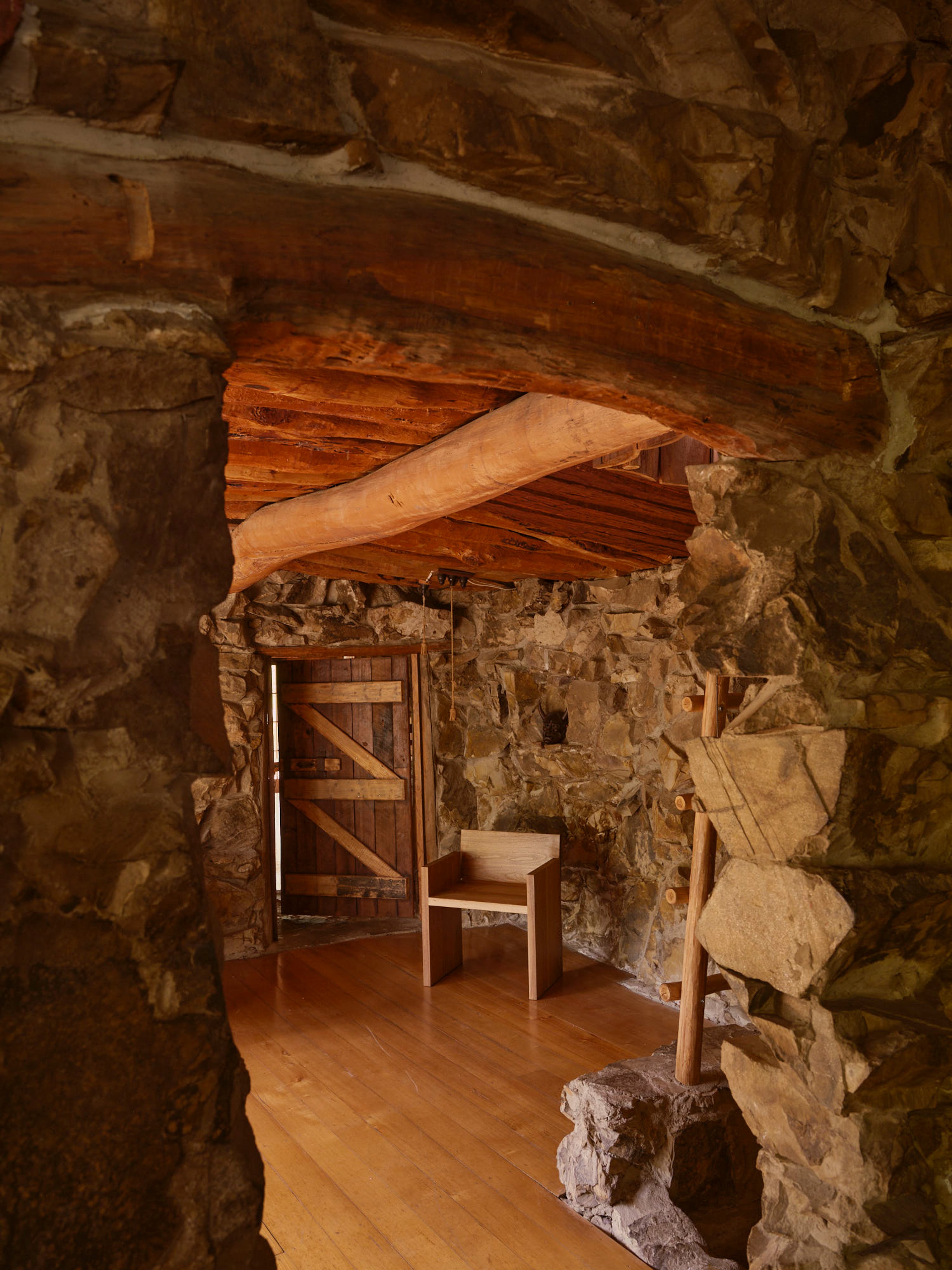 Looking through a stone door into a rustic stone-walled interior with a log timber ceiling and a timber door.
