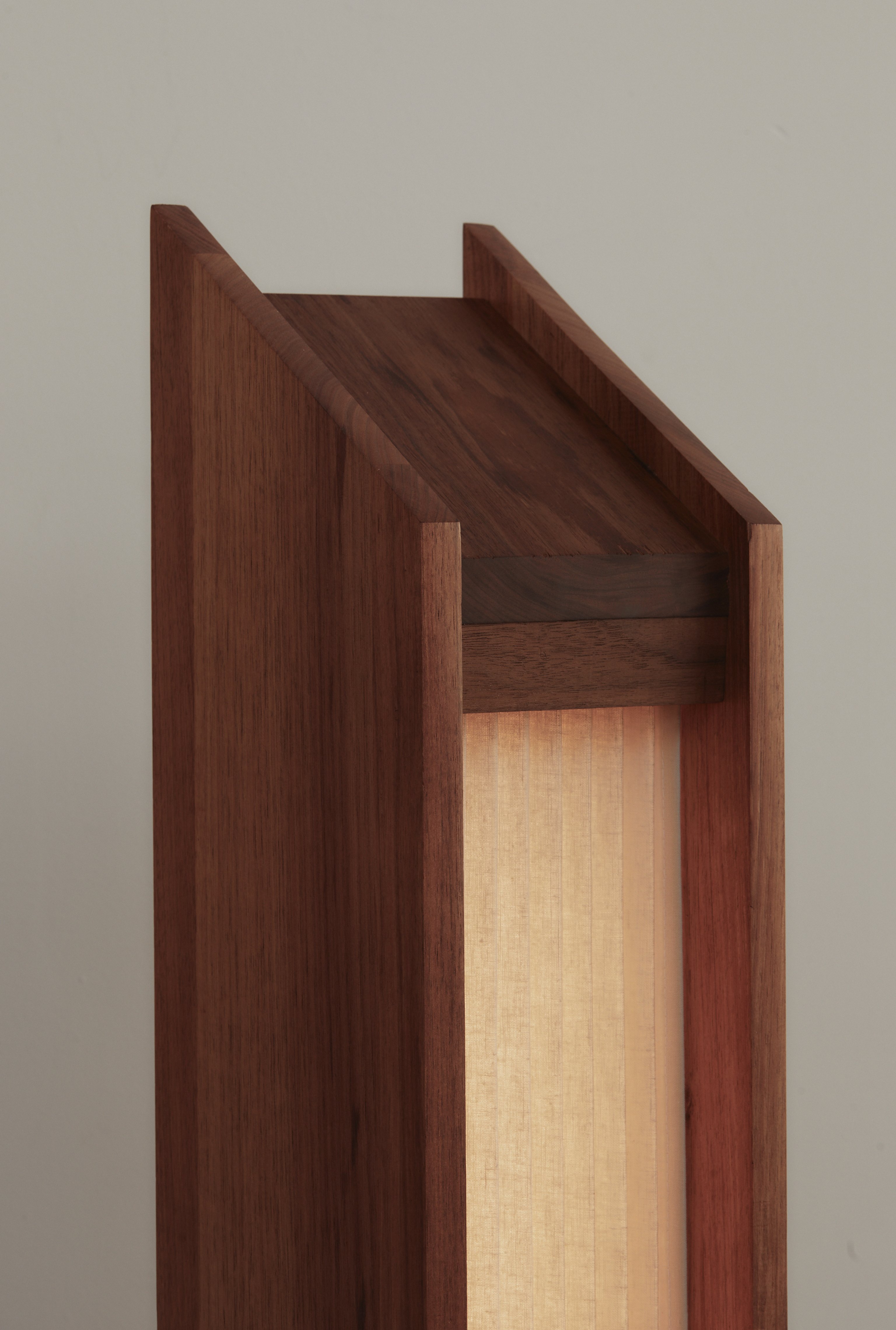 The triangular top of a timber and pleated linen floor lamp.