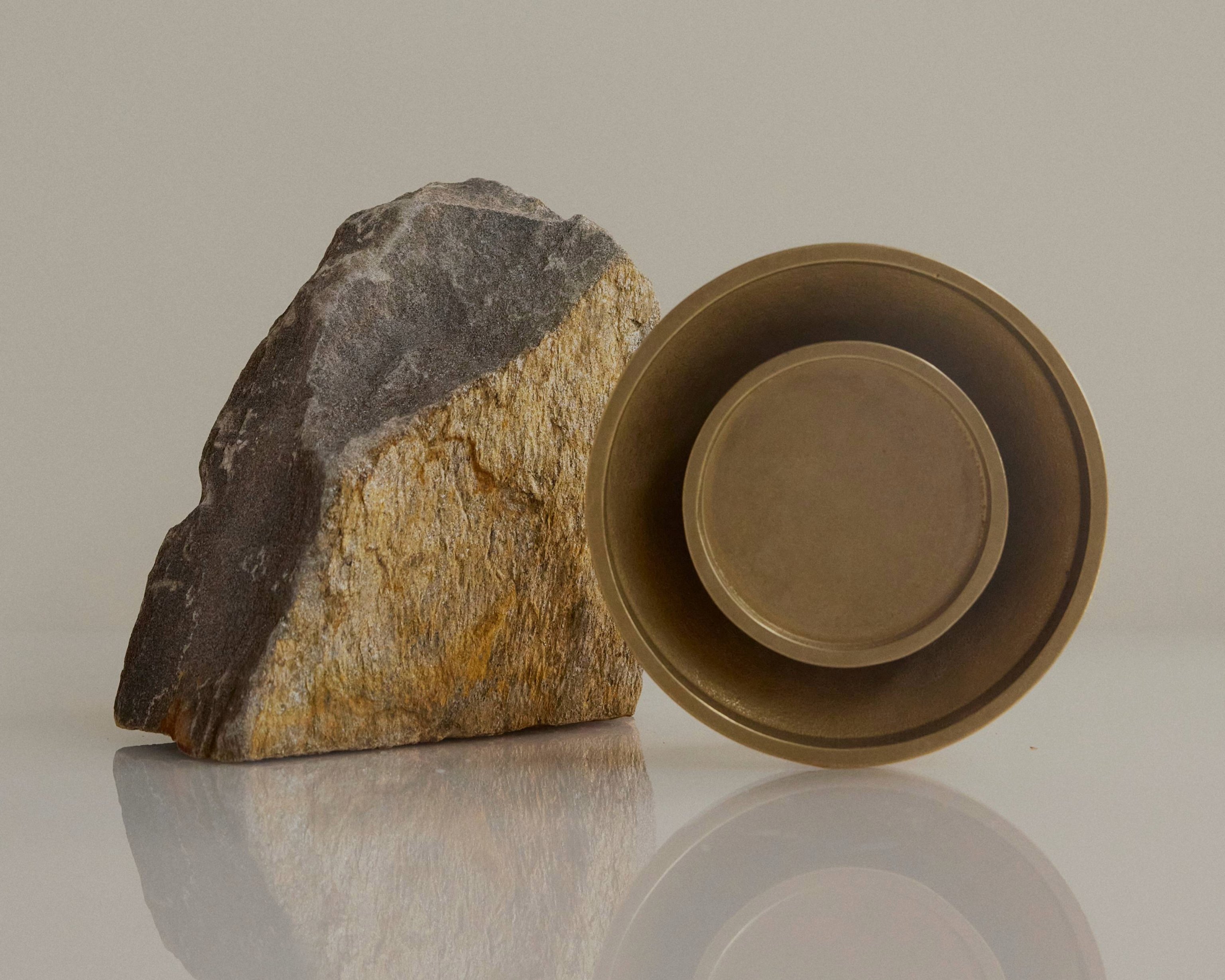 Chorus Wall Light in Brass, resting against a large rock.