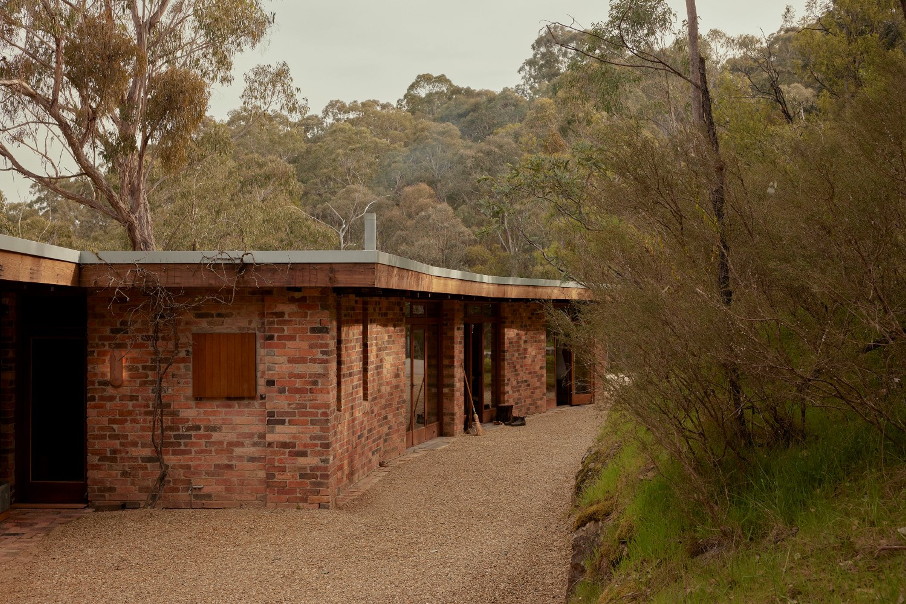 A low profile house made from red bricks. The house is surrounded by dense Australian bushland