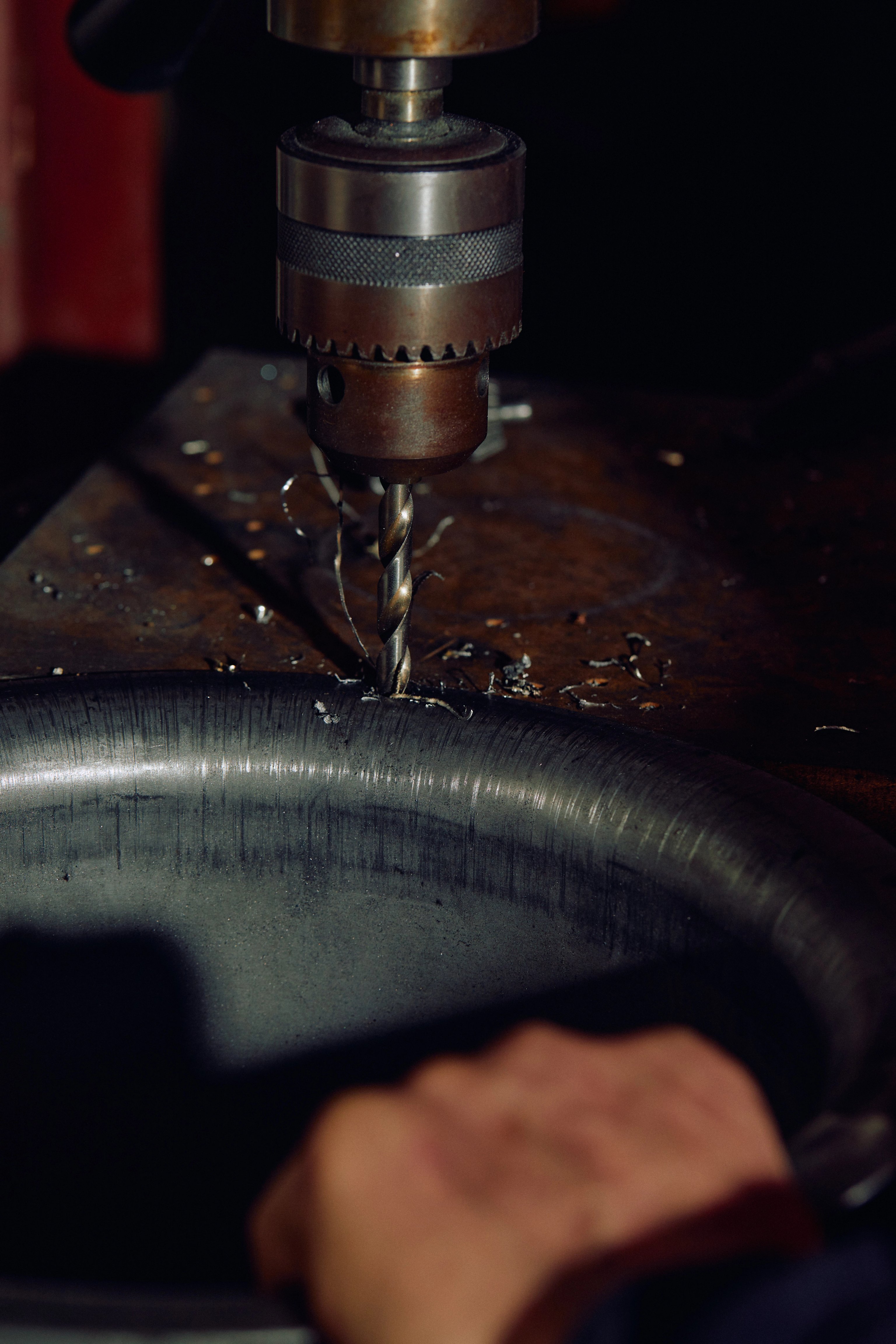 A drill press drilling holes in the rim of a metal drum