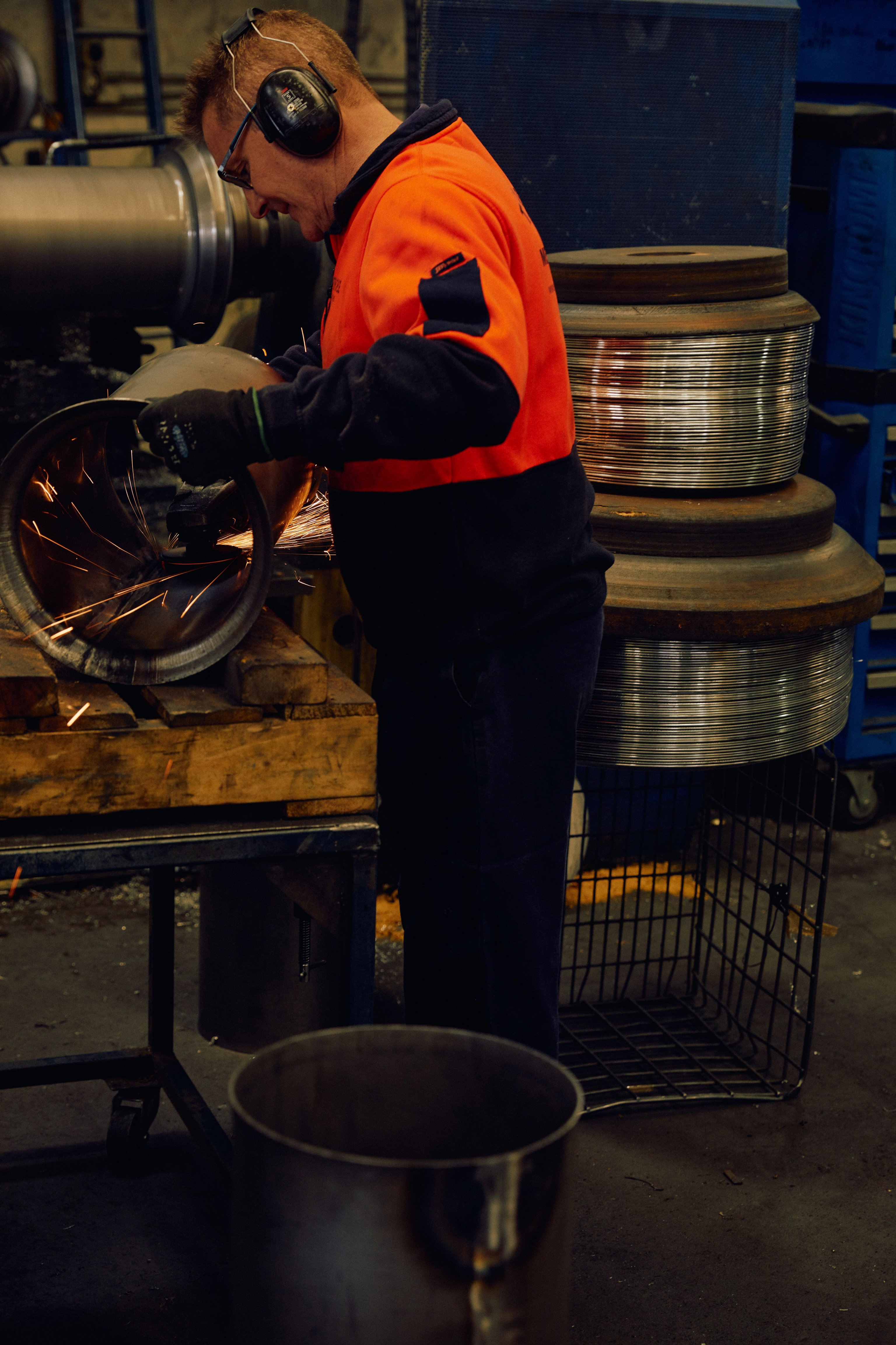 A man in high vis is inspecting a metal drum in a metal factory