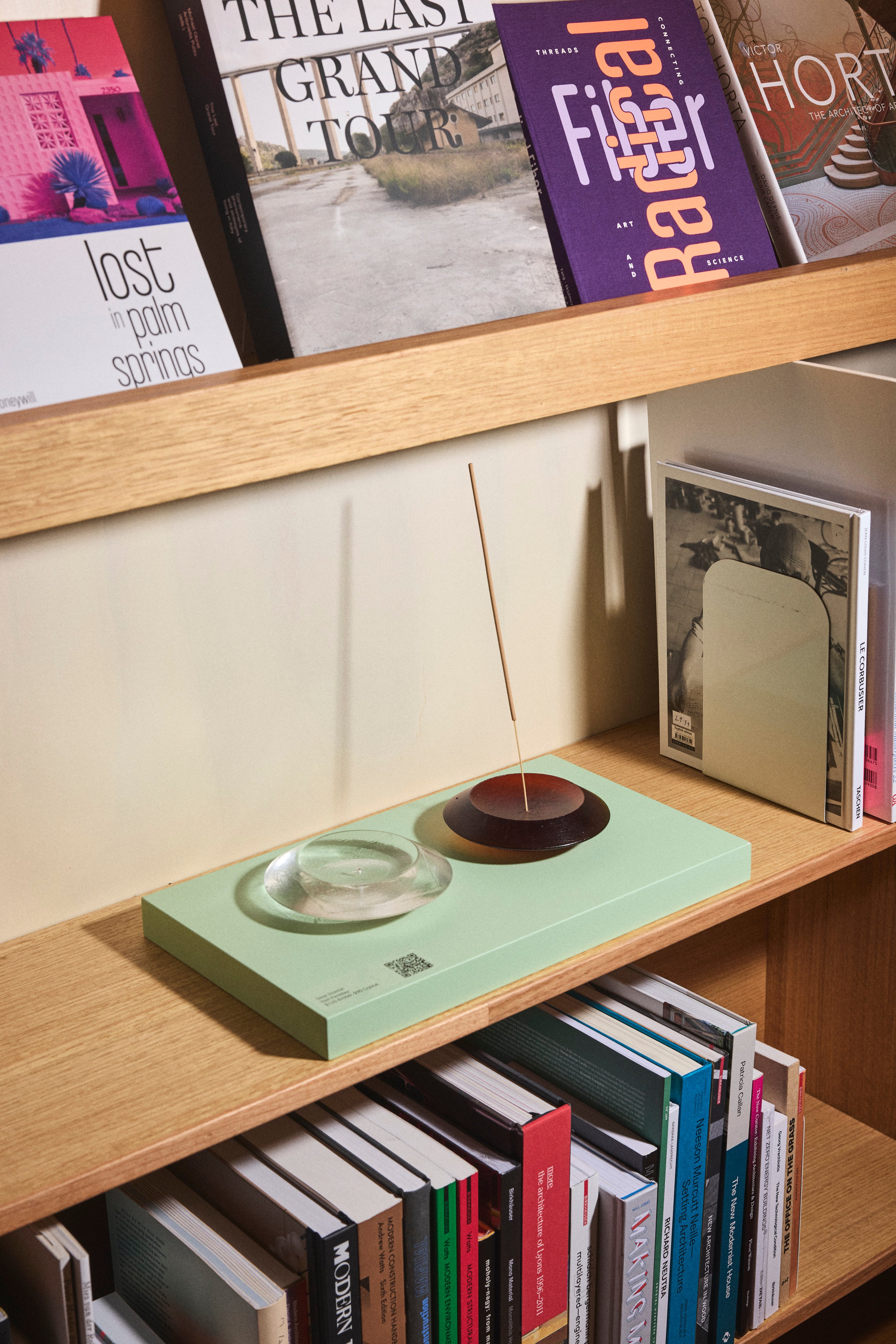 Two glass incense burners sitting on a pale green book in a bookshelf
