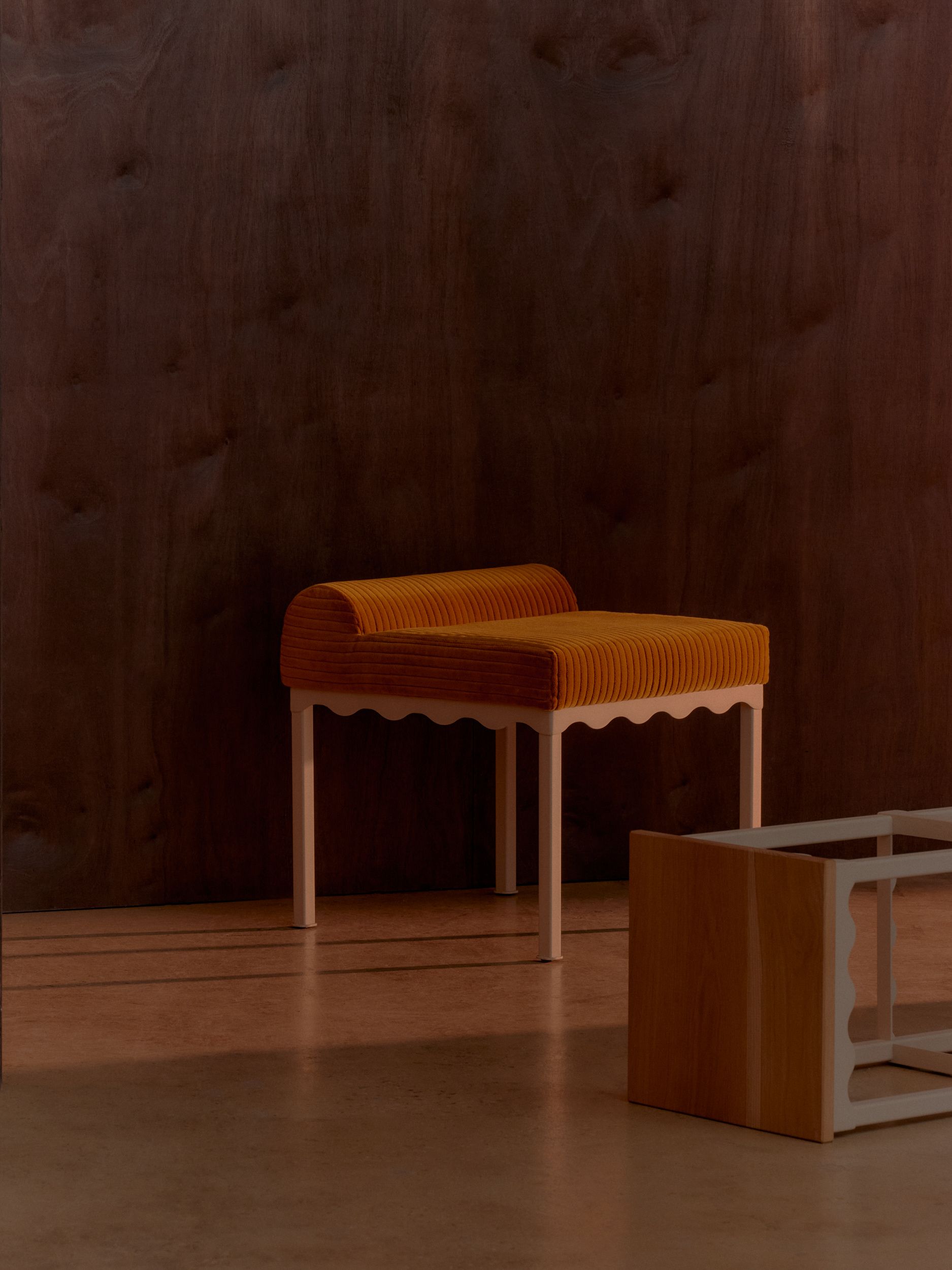 A yellow corduroy bench seat with a powder-coated frame that has a wavy trim detail. 