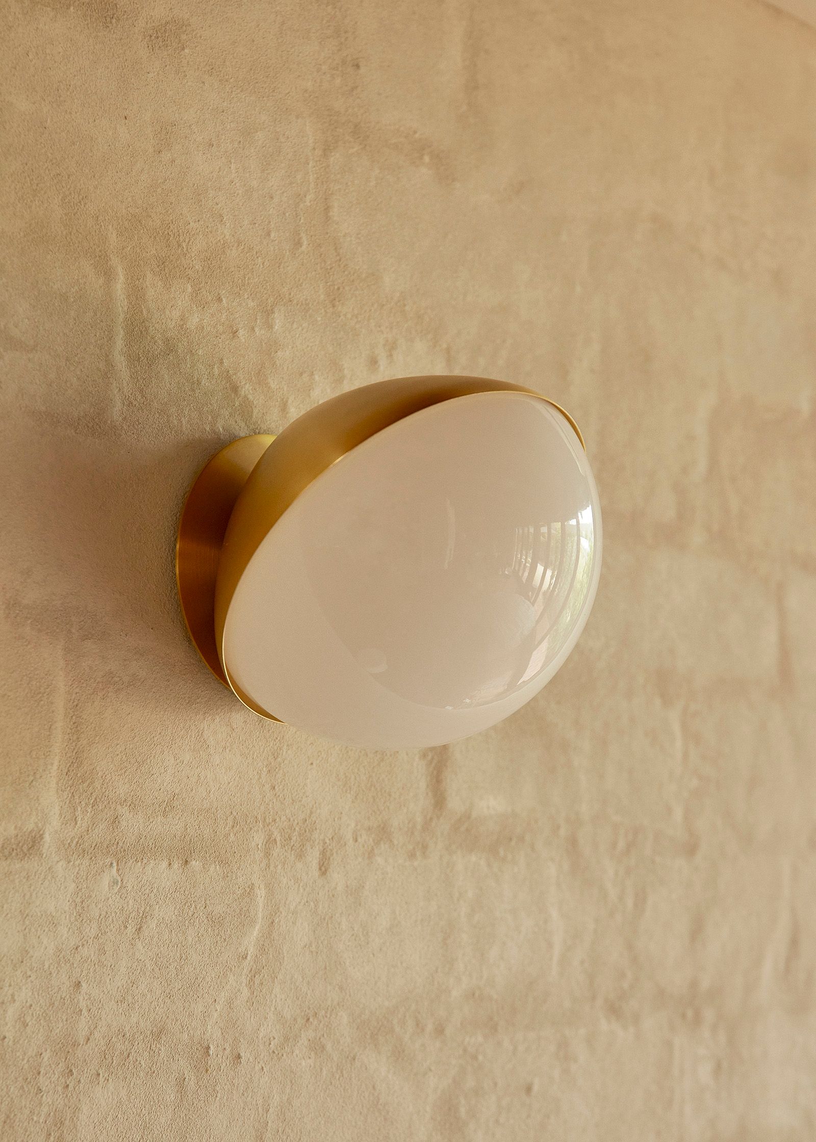 Jolly wall light in a brass finish fixed to a neural colour brick wall
