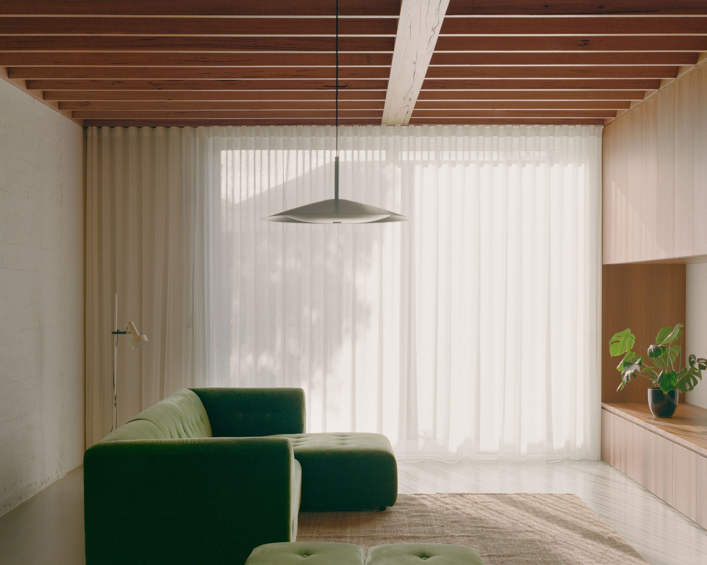 Burnley House by Field Office Architecture, featuring a eucalypt Broad Pendant and plush green sofa.