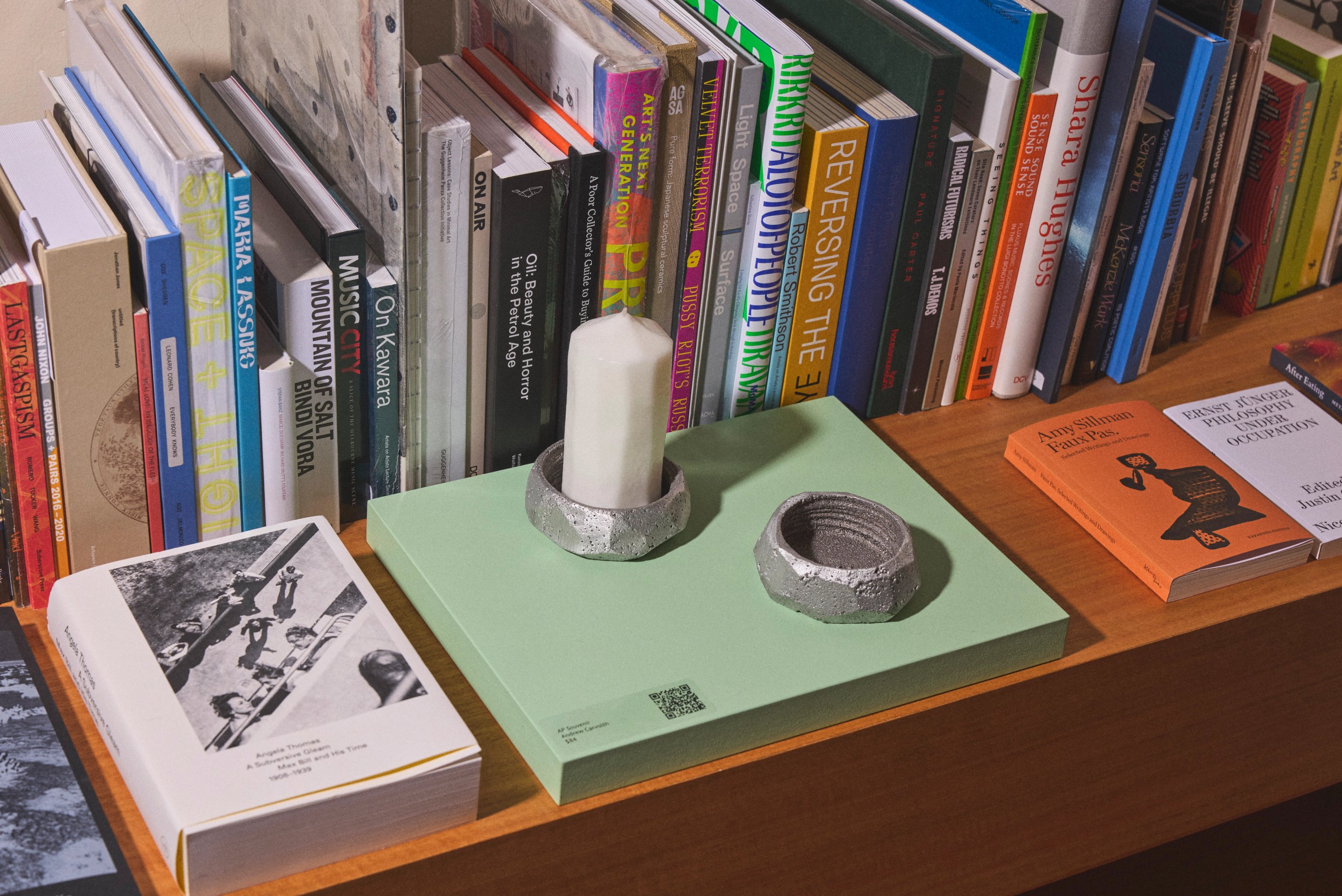 Thick white candle and metal candle holder sitting on a pale green book in a bookshelf surrounded by other books