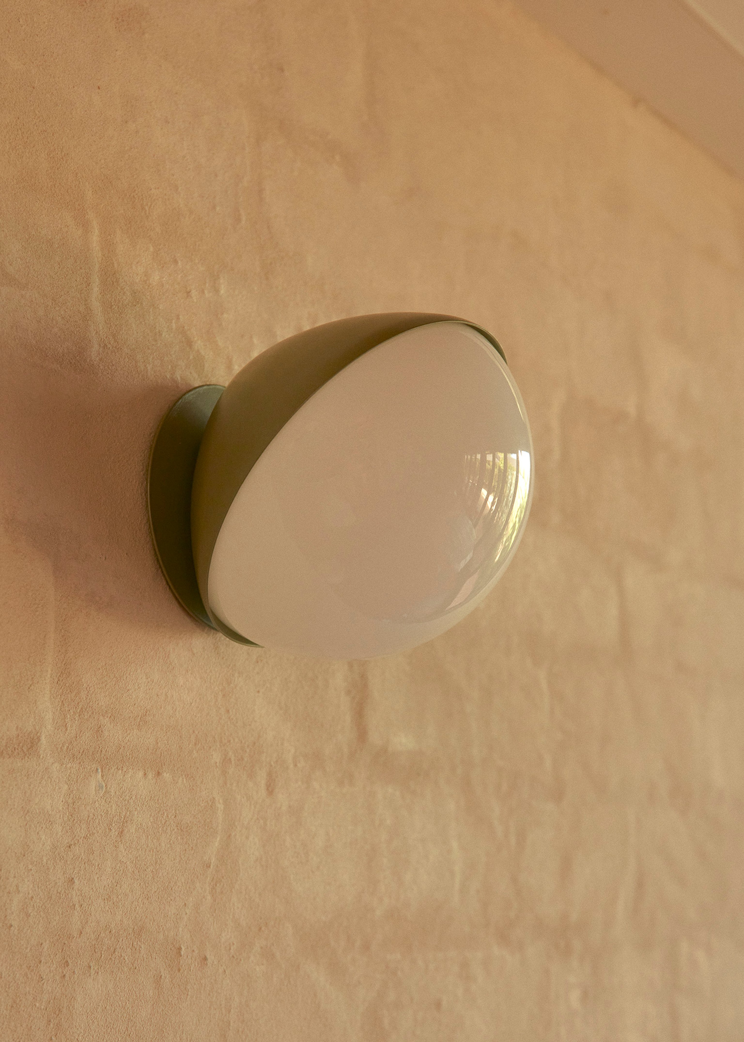 Jolly wall light in a eucalypt colour fixed to a neural colour brick wall