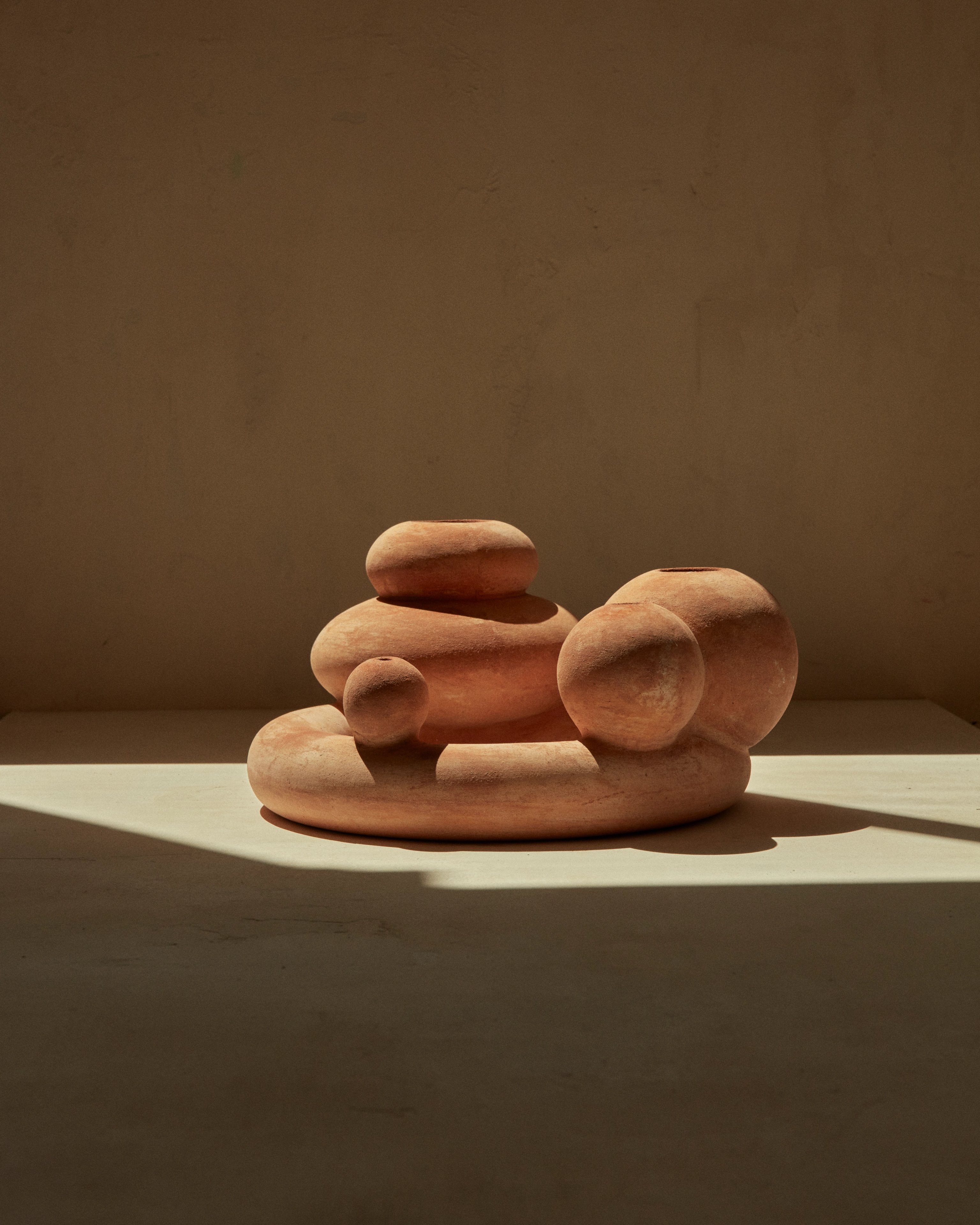 A terracotta object designed for New Volumes. Neutral background with with strong shadows