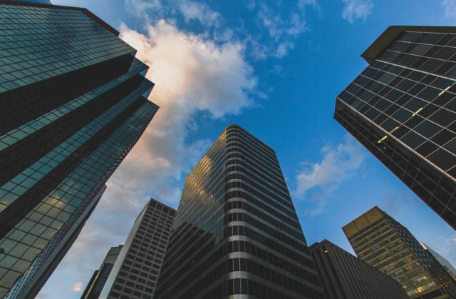 Black and blue skyscrapers beneath a partially-cloudy blue sky.