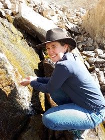 A person hiking holds her hands against a rock