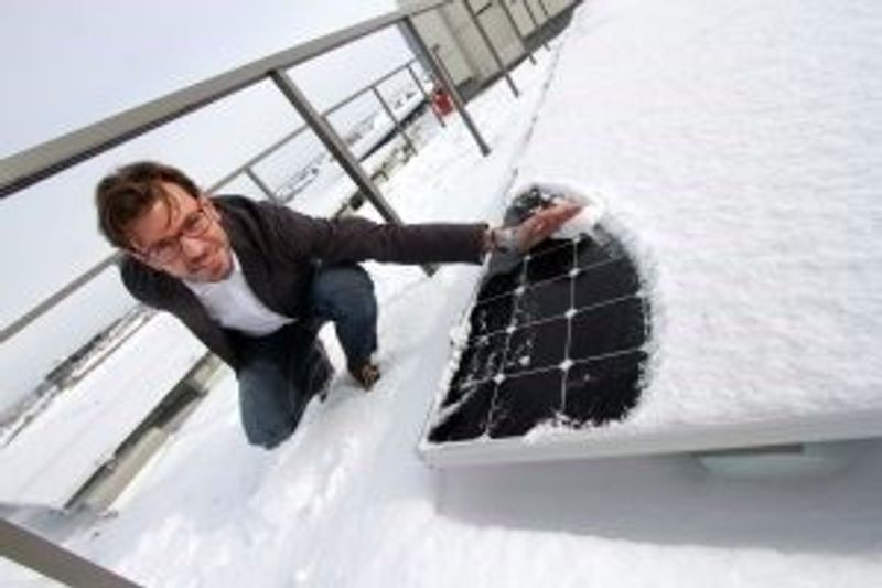 A man in a light sweater brushes snow off a solar panel with his bare hand