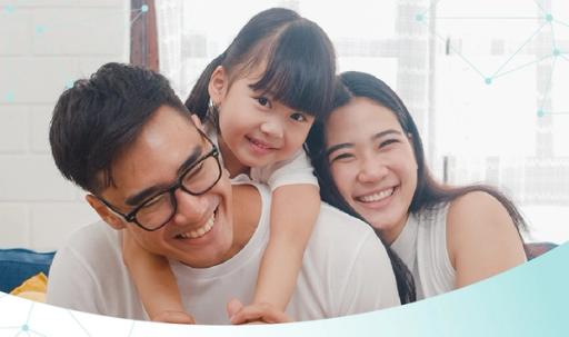 Two parents and a child smile and laugh next to a white brick wall and large window