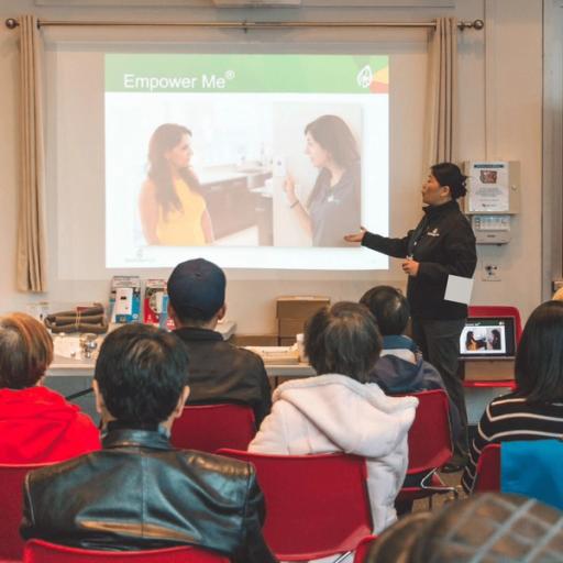 A woman in a black sweater presents next to a presentation board reading 'Empower Me'