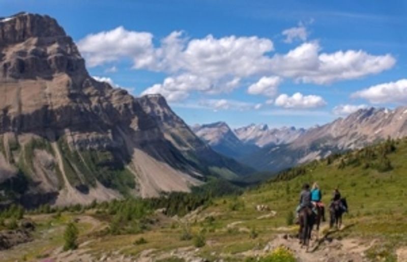 A group of people ride horses through the mountains