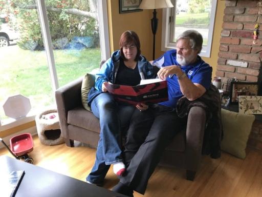 A man and woman sit on a loveseat, reviewing an Energuide folder near a sliding door