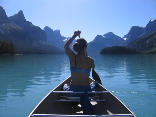 A woman paddles a canoe in a mountain lake under hazy skies