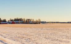 A frosty prairie field under a hazy sky, with a farm in the distance.