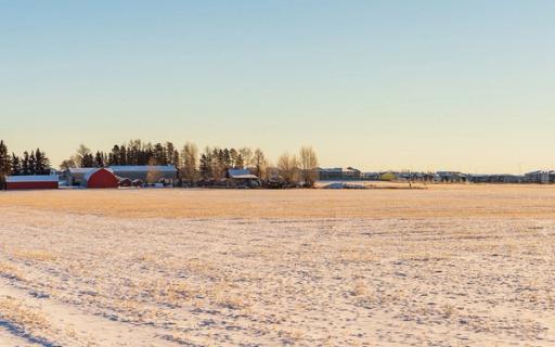 A frosty prairie field under a hazy sky, with a farm in the distance.