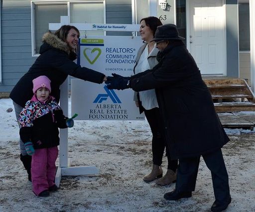 A woman with a child wearing a pink toque shakes hands with representatives from Habitat for Humanity in front of a new home.