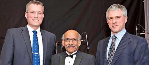 Three men wearing suits smile for the camera against a black backdrop.