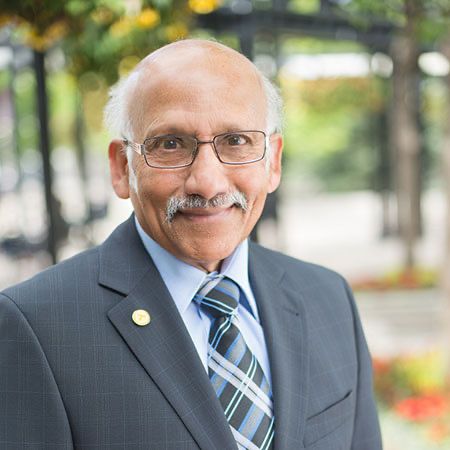 Charlie Ponde headshot, with a blurry backdrop of green trees and orange flowers.