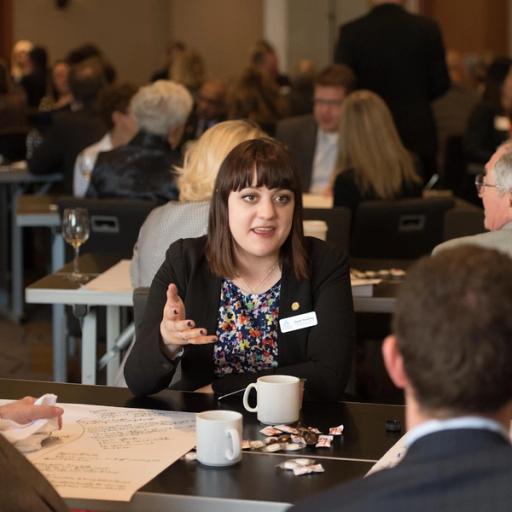 A woman with a nametag reading "Sarah" communicates with team members over coffee