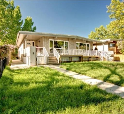 A duplex bungalow with tall grass out front, under a blue sky